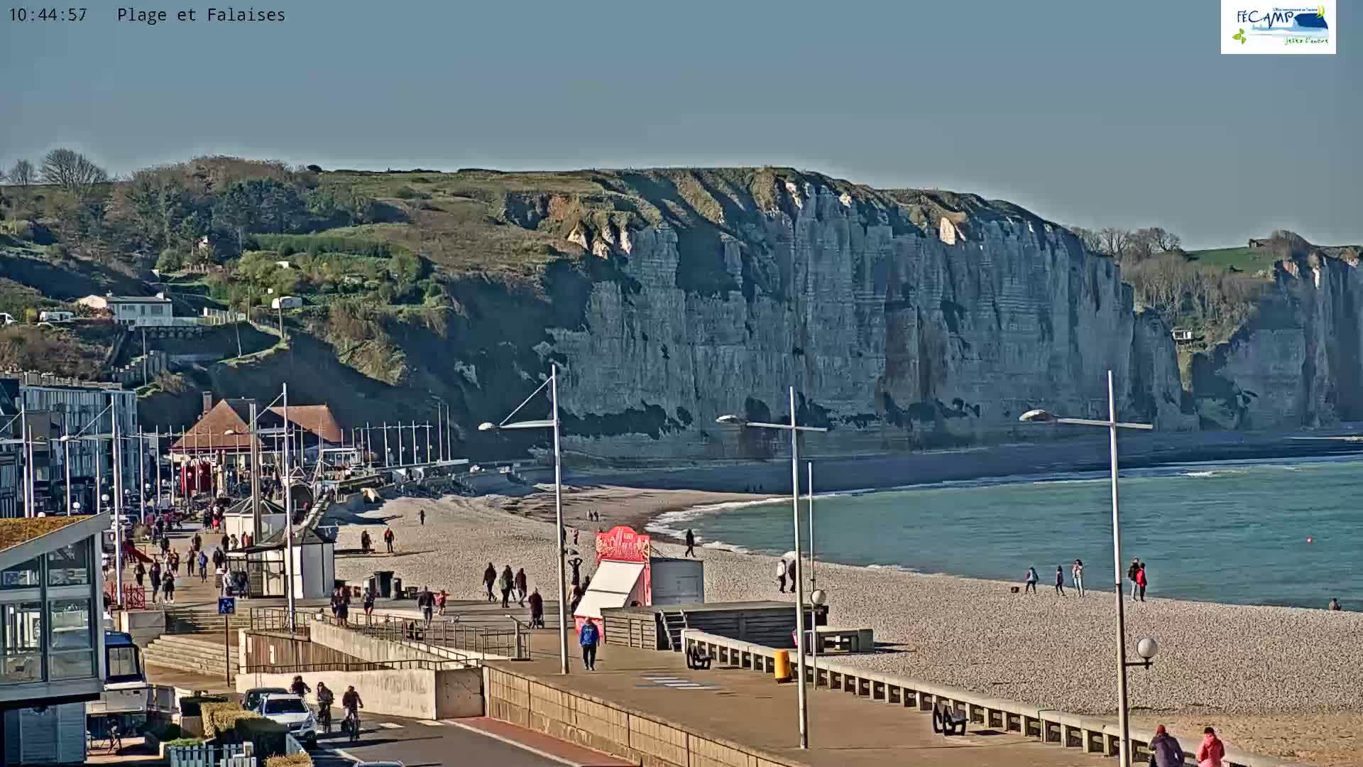 A sunny day at a pebble beach with a boardwalk and tall white cliffs in the background.
