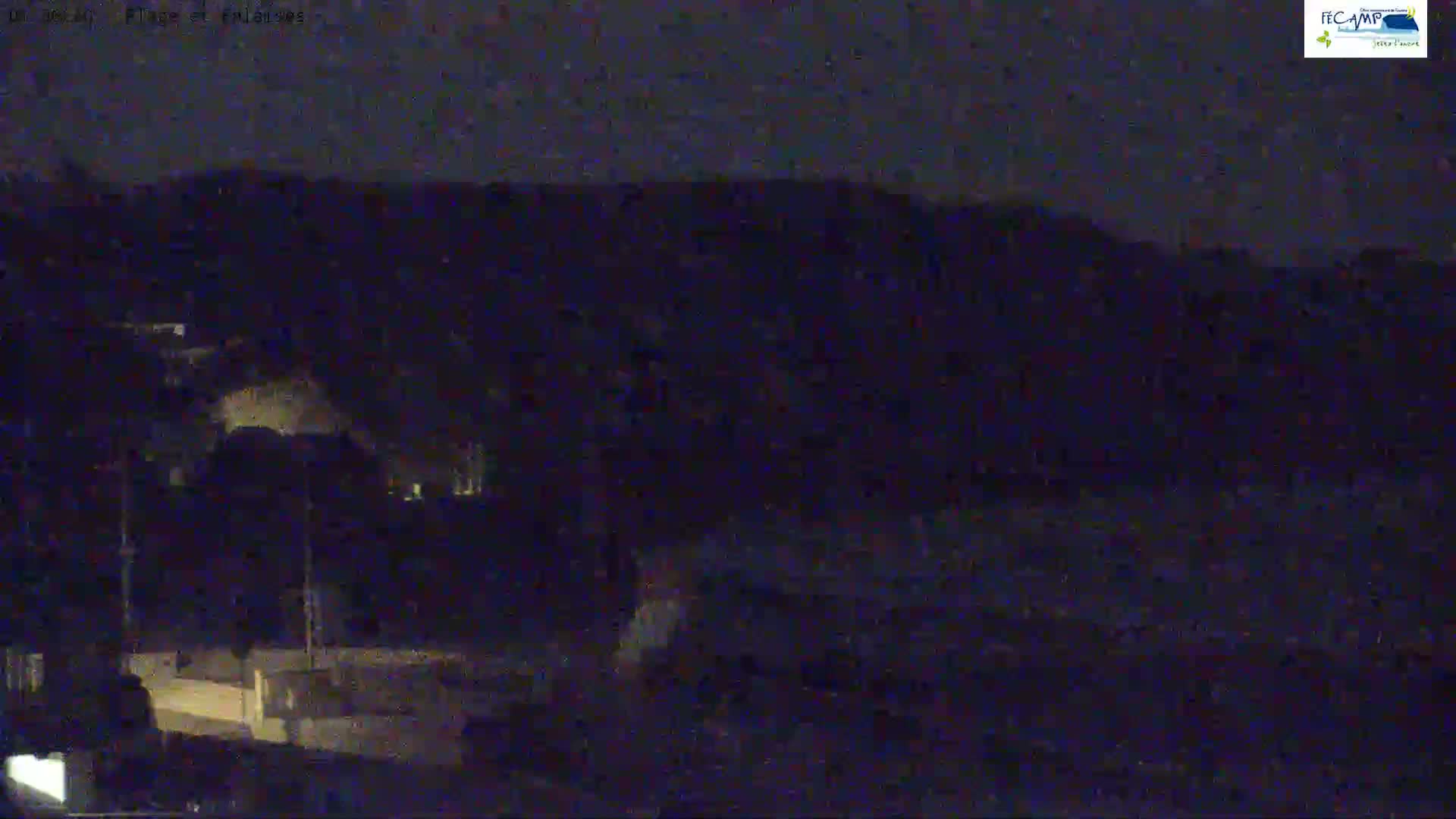 A dark nighttime scene shows dimly lit land and a dark body of water under a mostly clear sky.