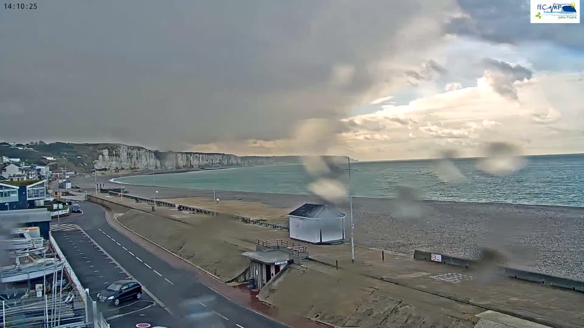 A nighttime view shows a beach, a walkway leading to a harbor with a lit lighthouse, under a clear, dark sky.