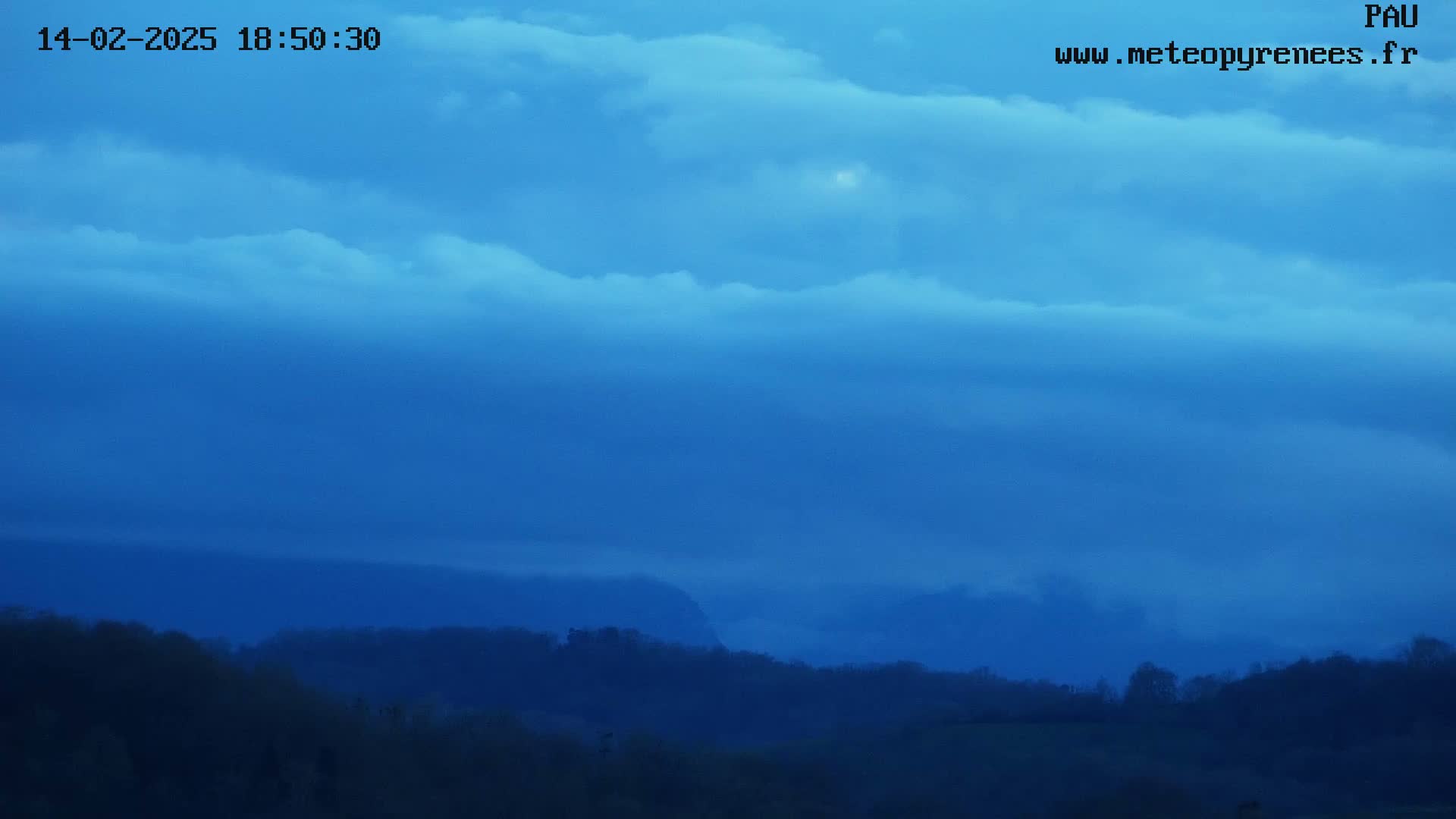 A dark blue sky filled with clouds sits over a low-lying, dark, hilly landscape.
