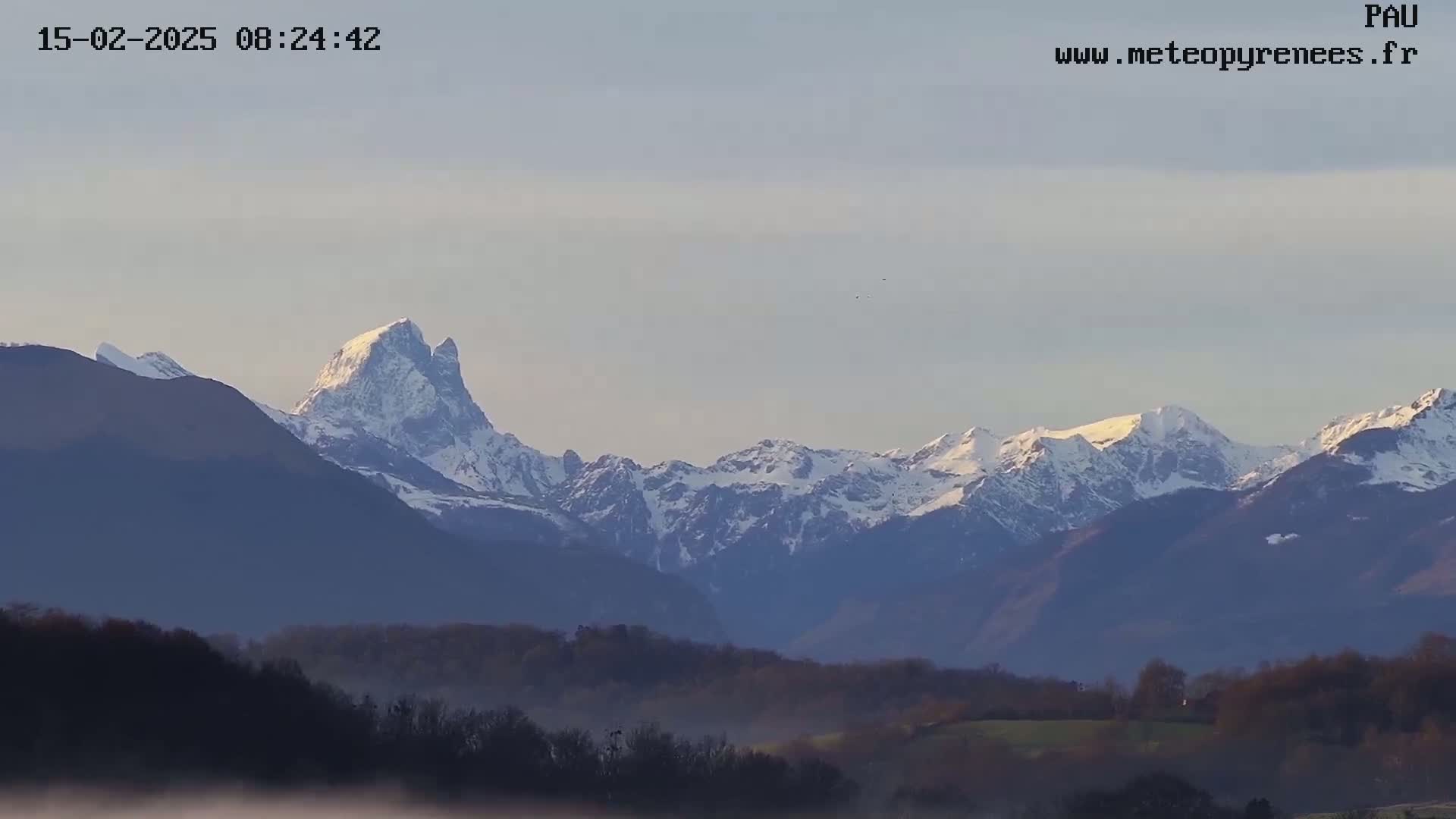 A snow-capped mountain range is visible in the distance, with a layer of fog or mist in the foreground under a clear, light-grey sky.