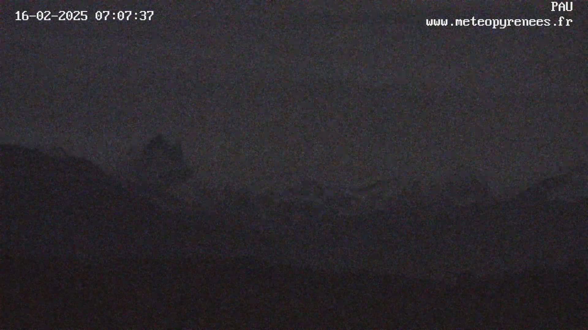A dark, nighttime view of a hilly or mountainous landscape under a mostly clear, dusky sky.
