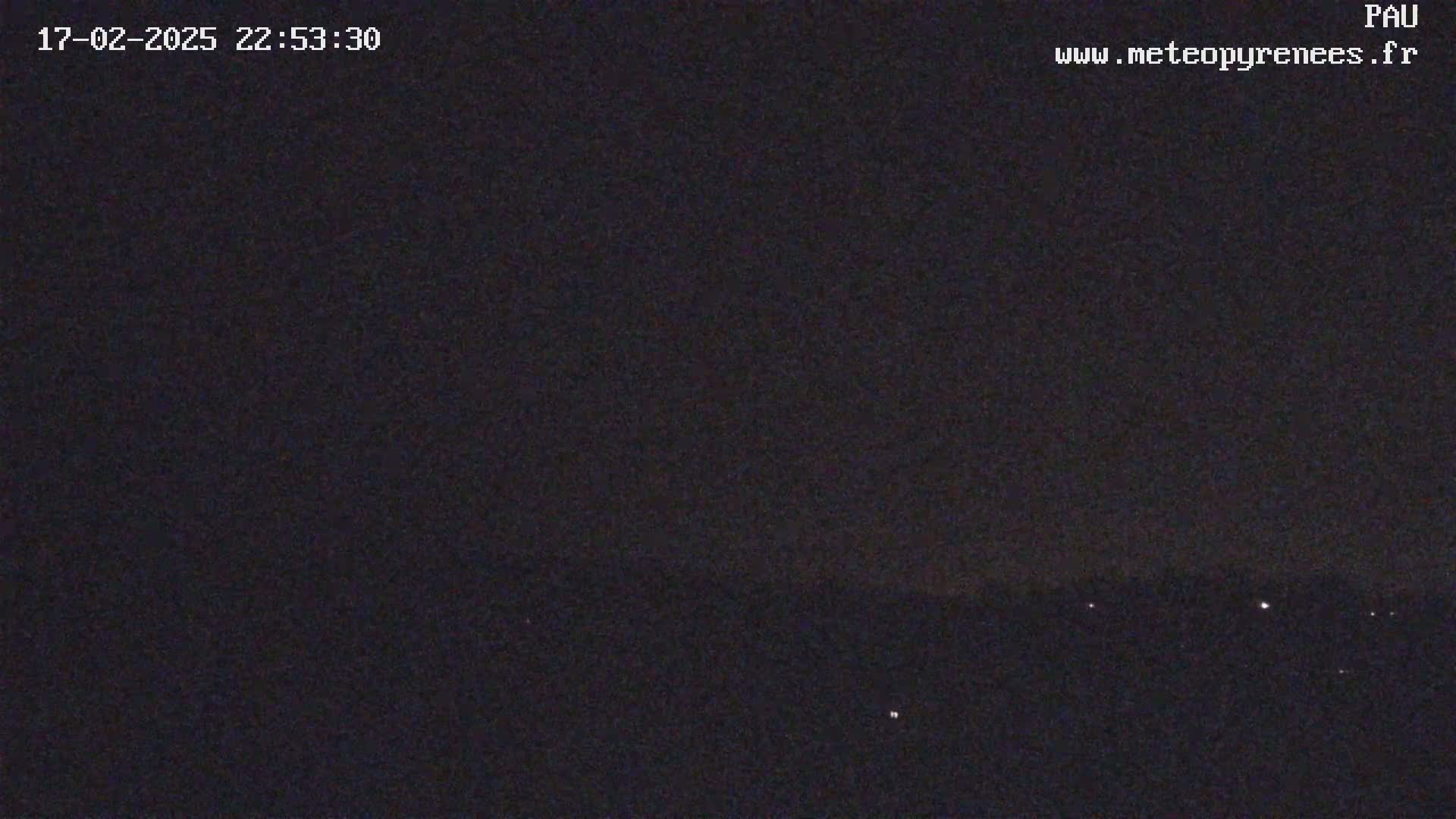 A nighttime, dark image shows a few small, distant lights on the horizon under a clear, dark sky.