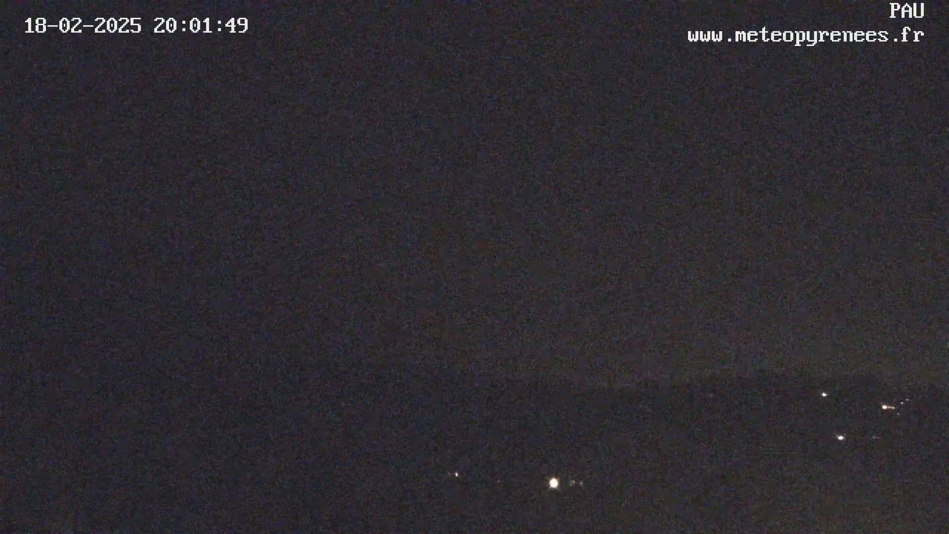 A nighttime long shot shows a dark, mostly clear sky over a distant, dimly lit landscape.