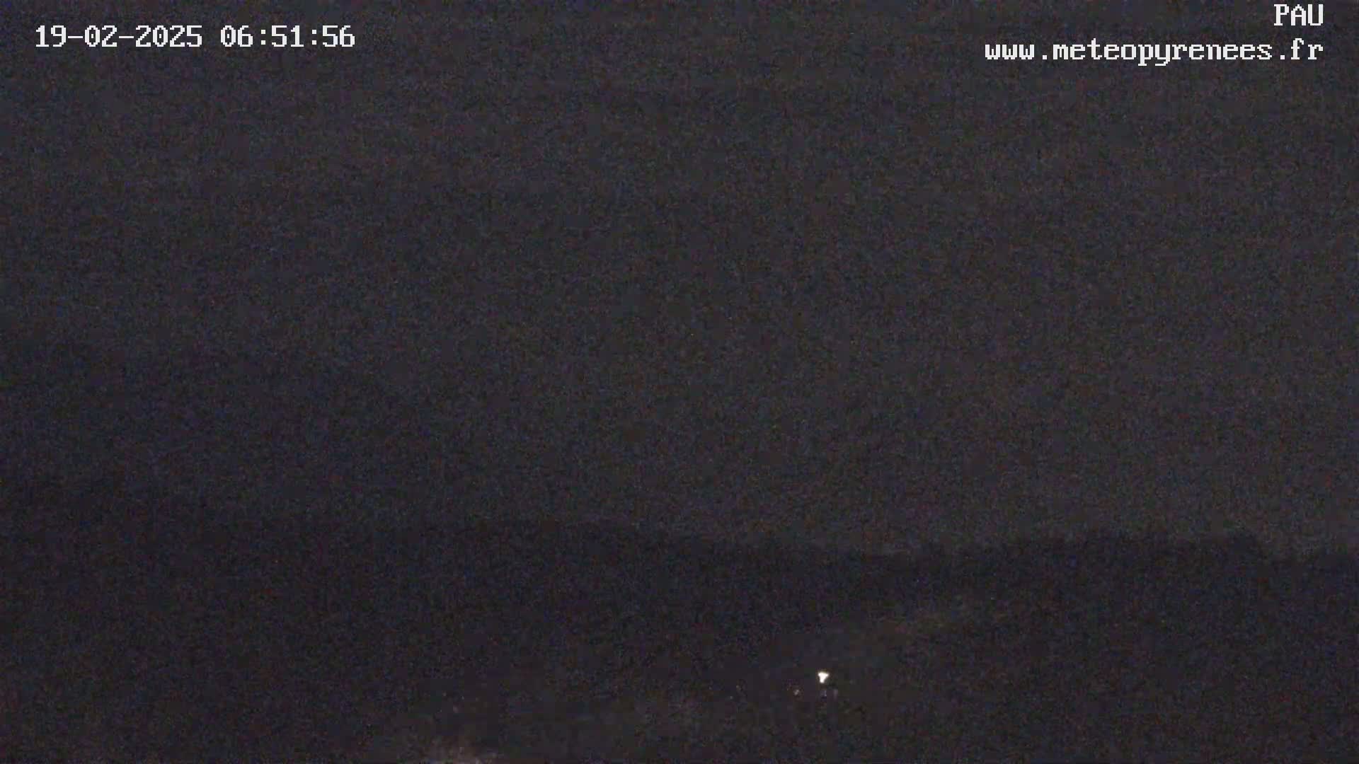 A dark, nighttime scene shows a mostly clear sky over a distant, dimly lit landscape.