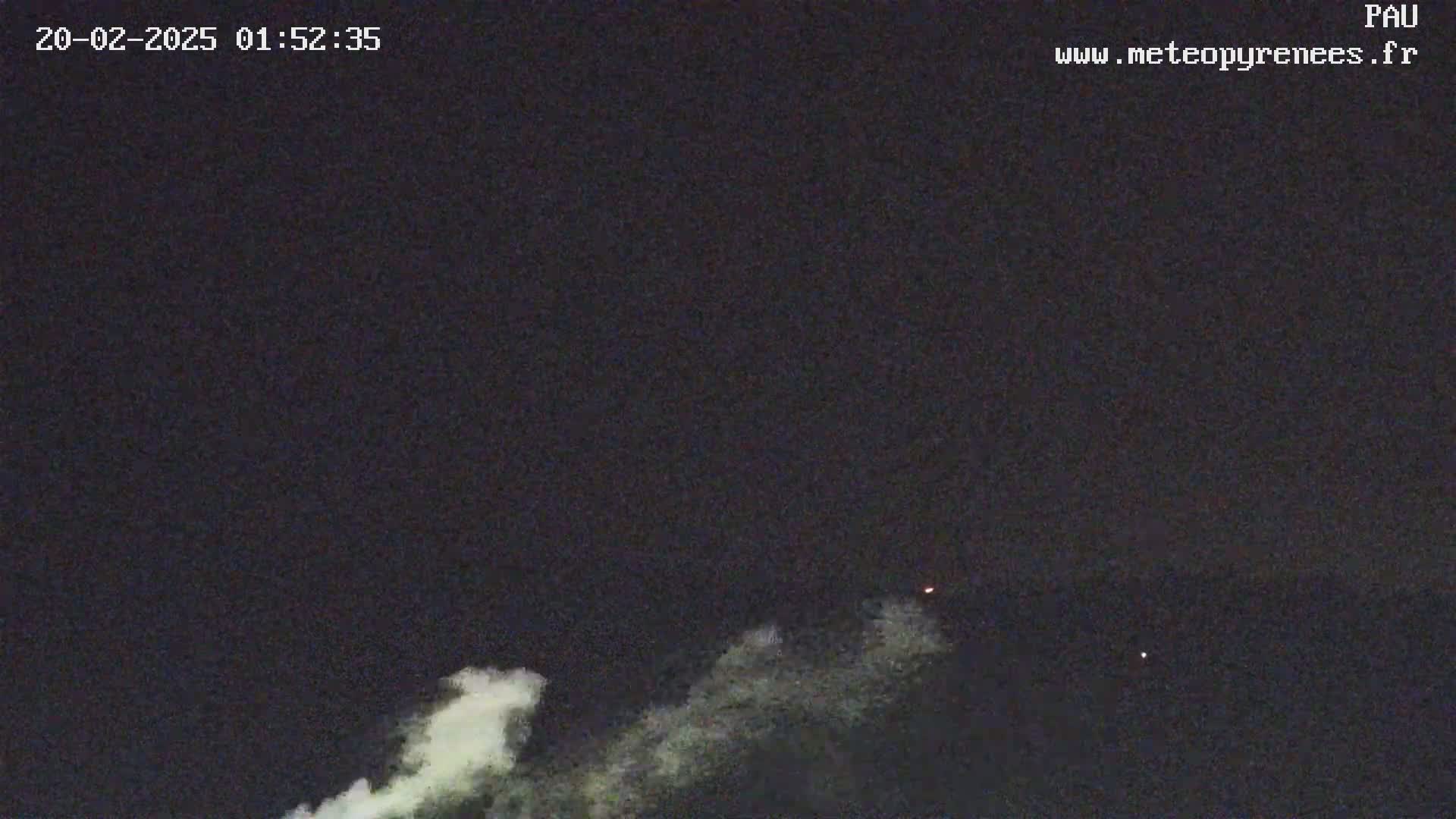 A nighttime outdoor image shows a plume of white smoke or cloud against a dark sky with a few faint red lights visible.