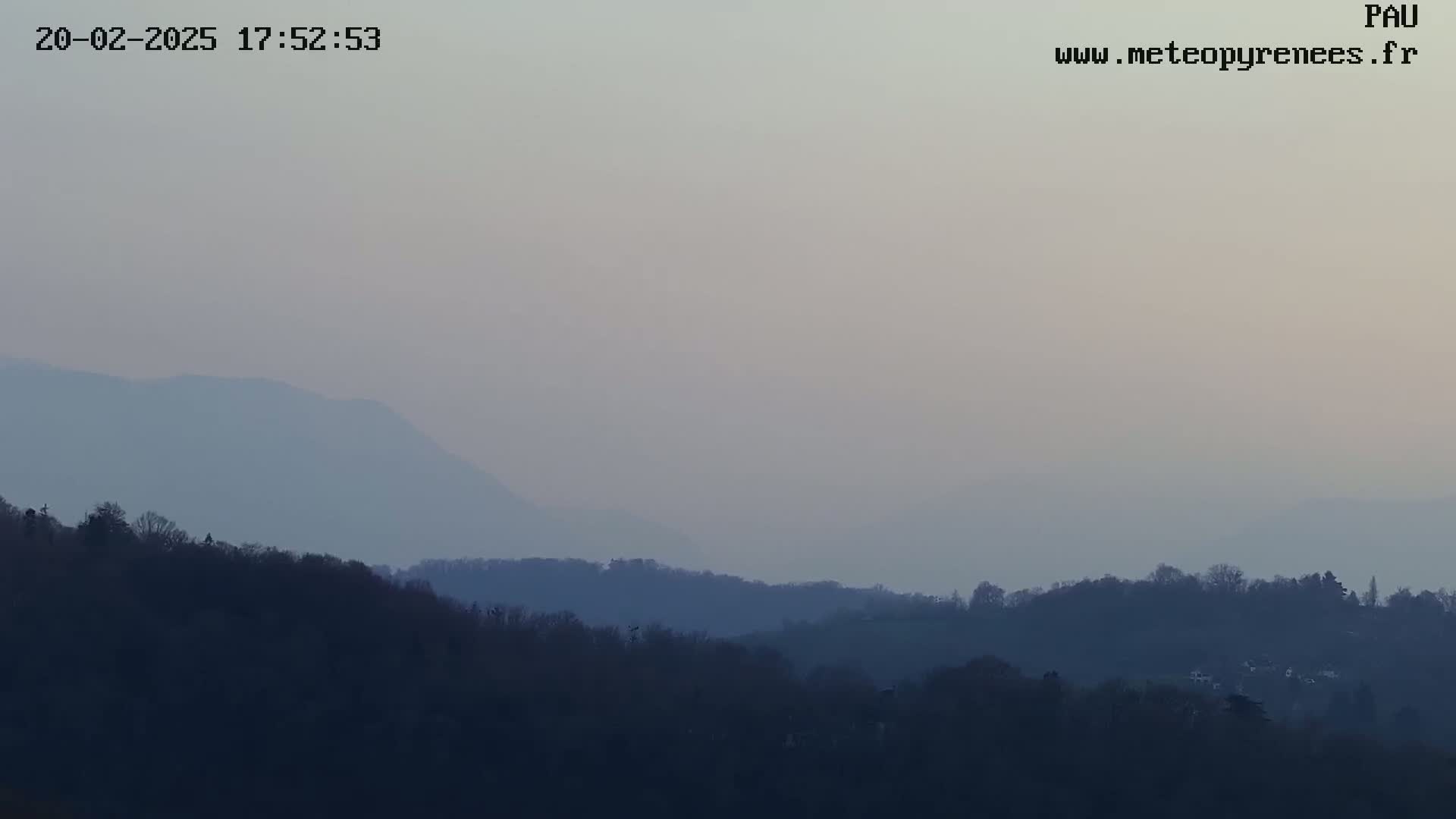 A hazy, dusky view shows layers of dark-colored hills and trees extending to a pale horizon under a muted sky.