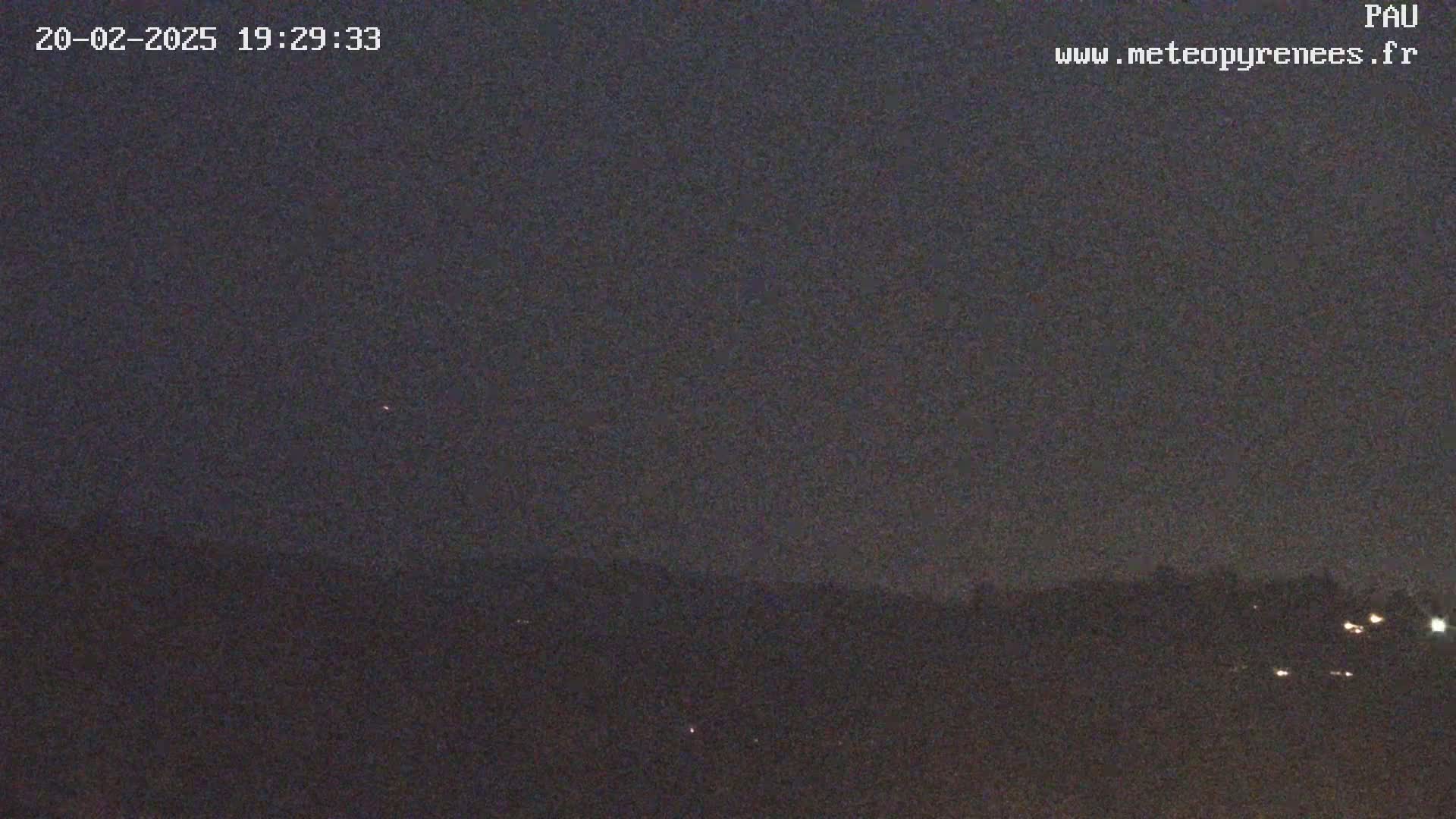 A nighttime, dark image shows a distant line of trees and lights under a mostly clear, dark sky.