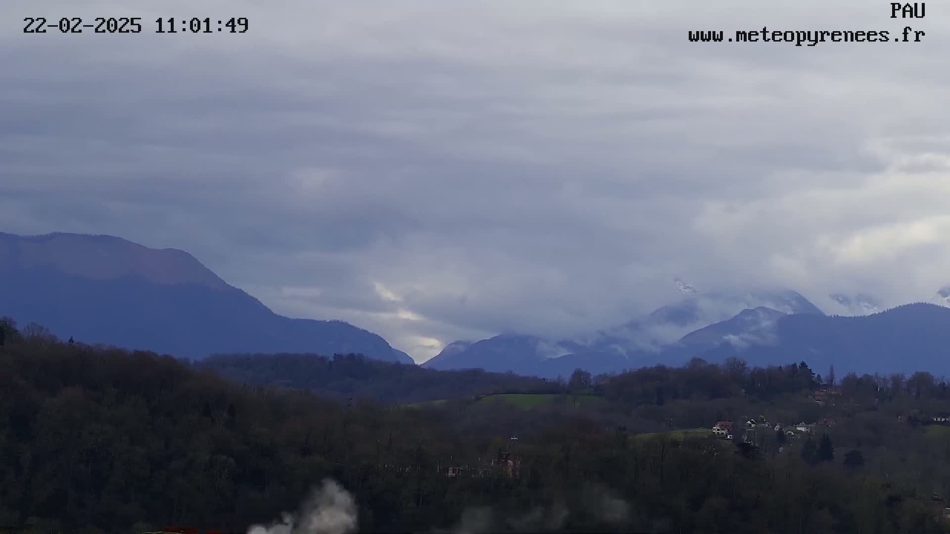 A cloudy day reveals a landscape of rolling hills and distant mountains, some of which appear to have snow on their peaks.