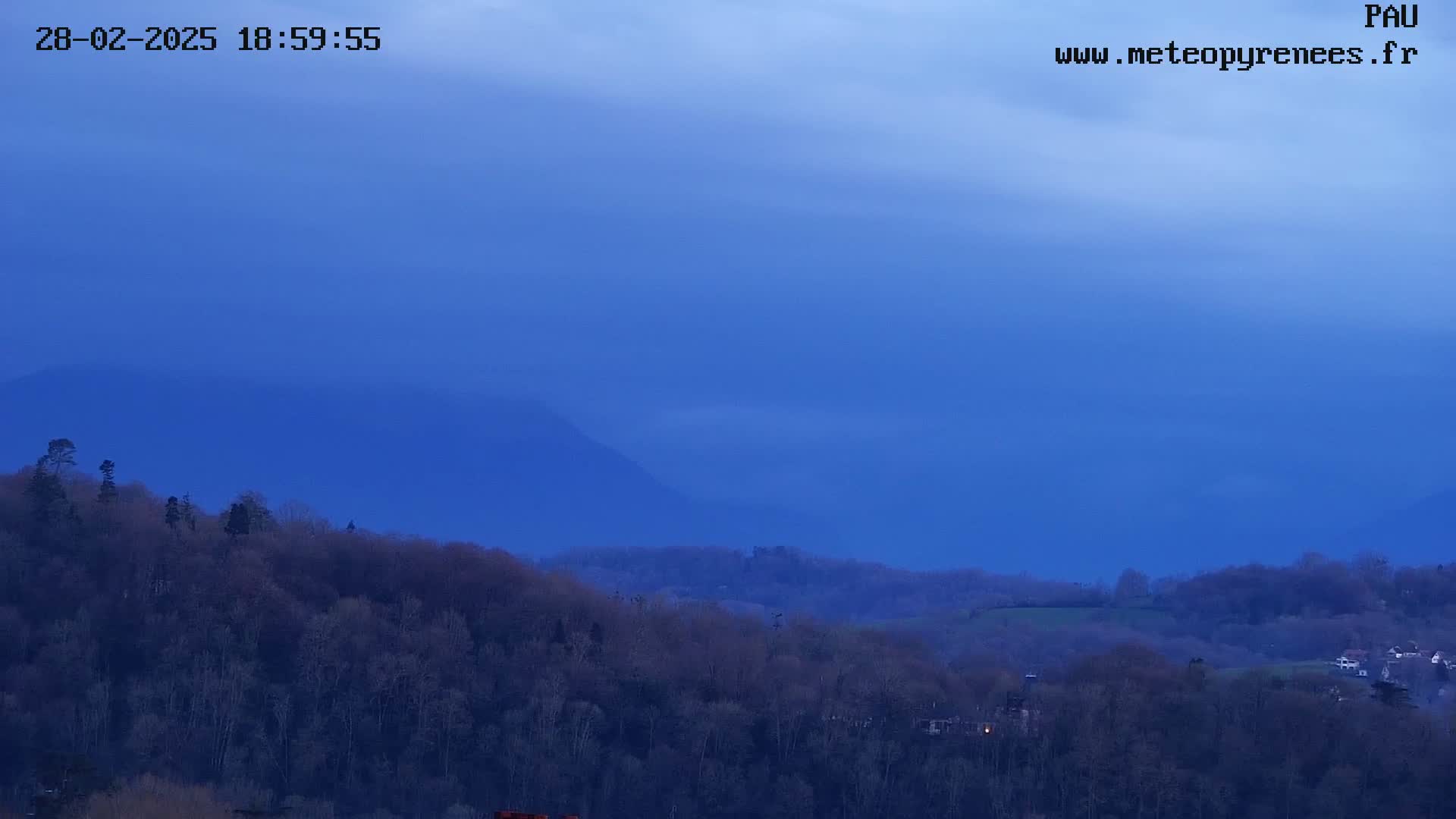 A hazy, blue twilight sky overlooks a landscape of dark, leafless trees and distant, shrouded mountains.