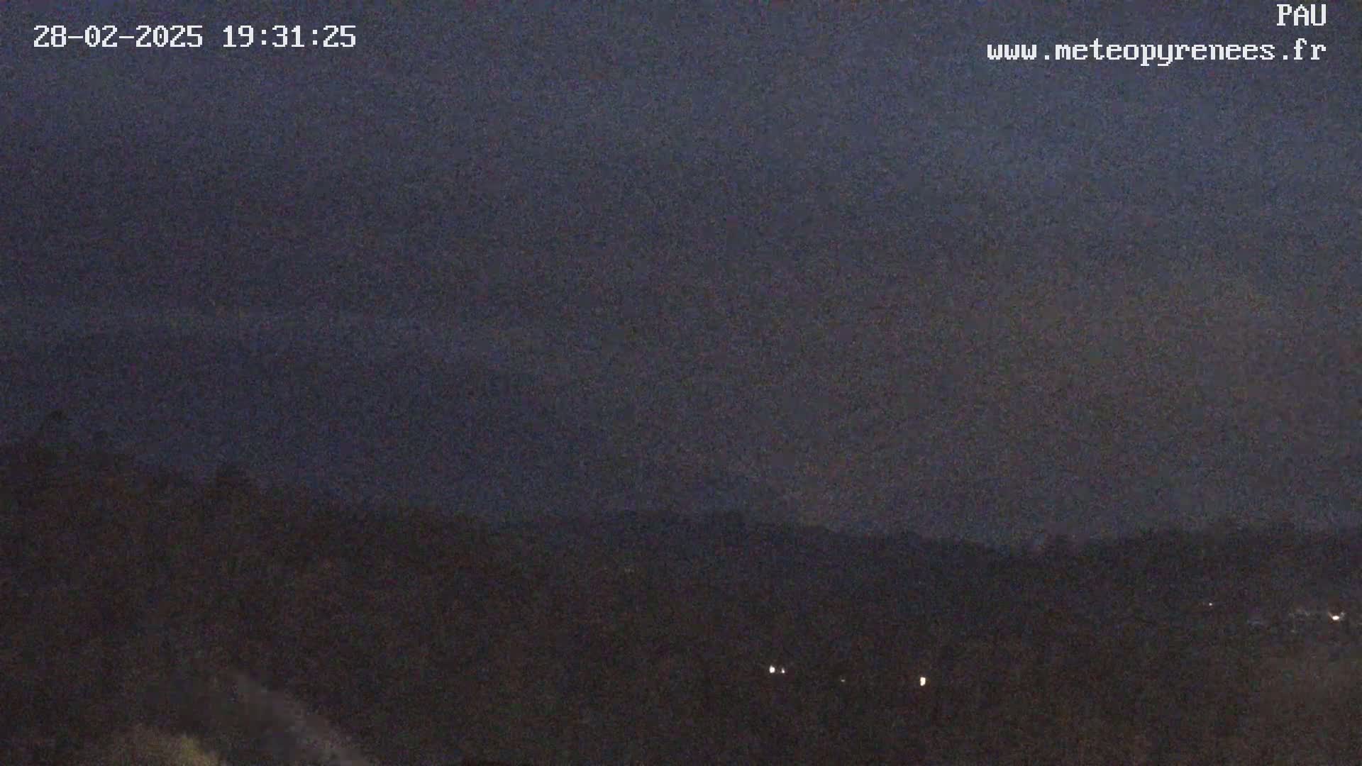 A dark, nighttime landscape is visible, showing a distant line of hills under a mostly clear, dusky sky.