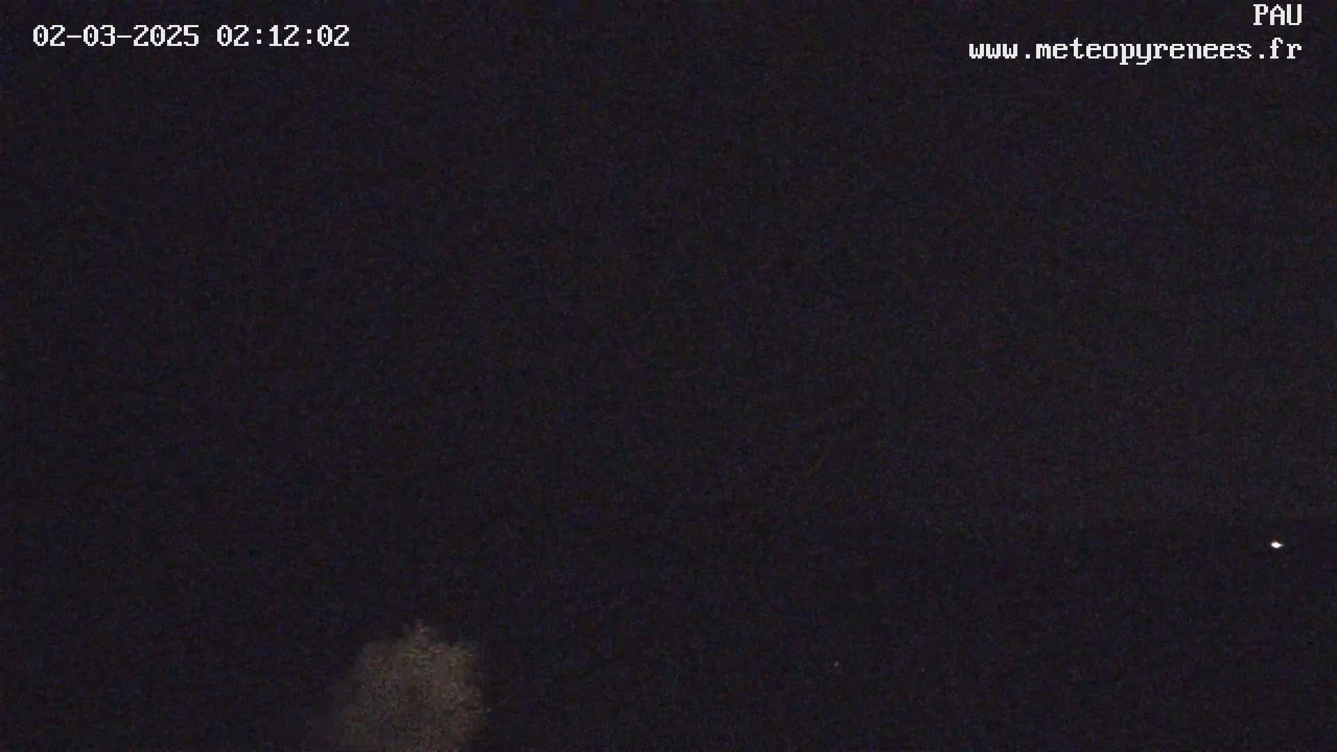 A nighttime, dark sky shows a faint, low cloud or fog at the bottom of the frame, with a few distant, faint lights visible.