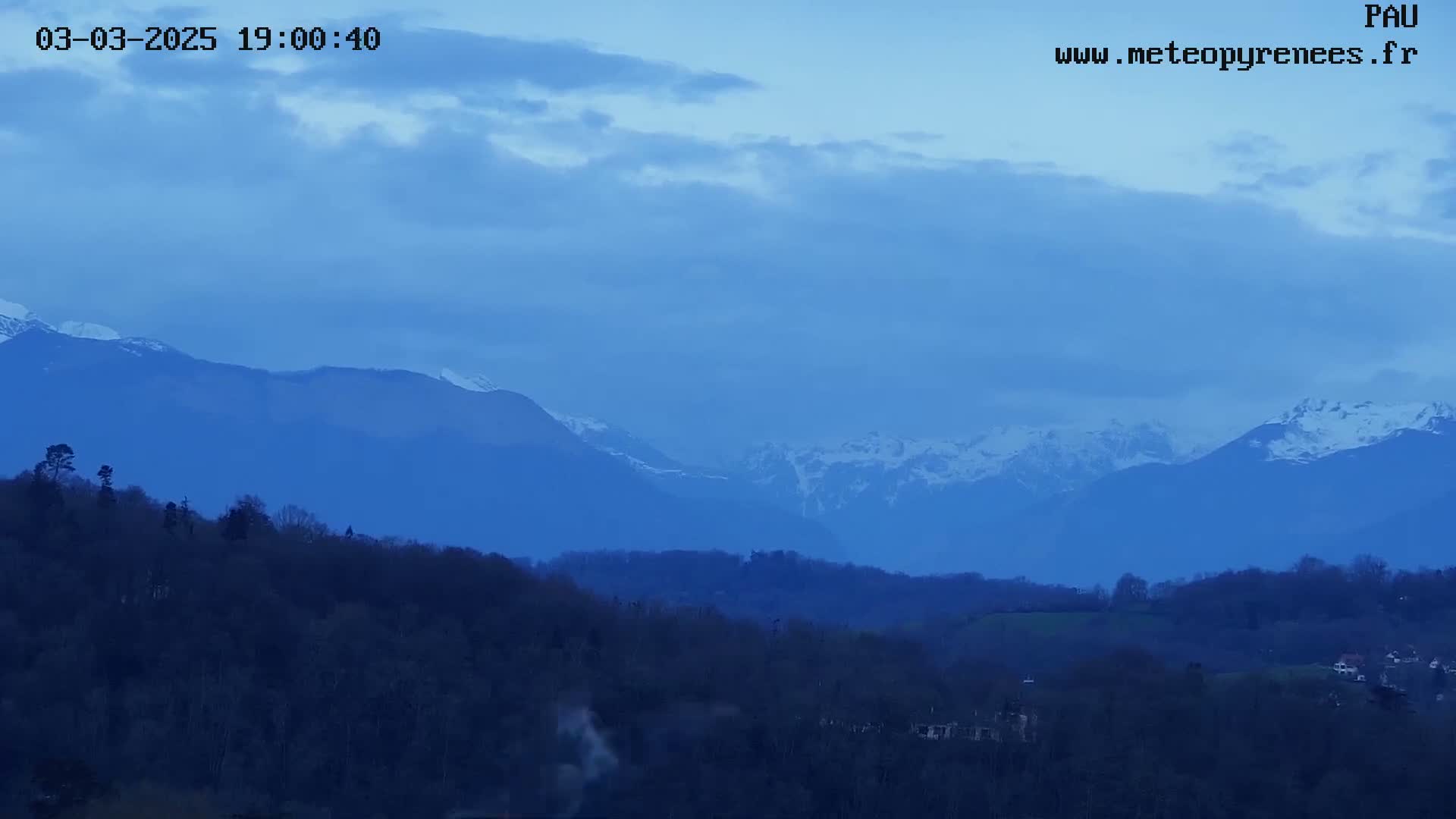 Snow-capped mountains are visible in the distance behind a dark, rolling hillside under a twilight sky.