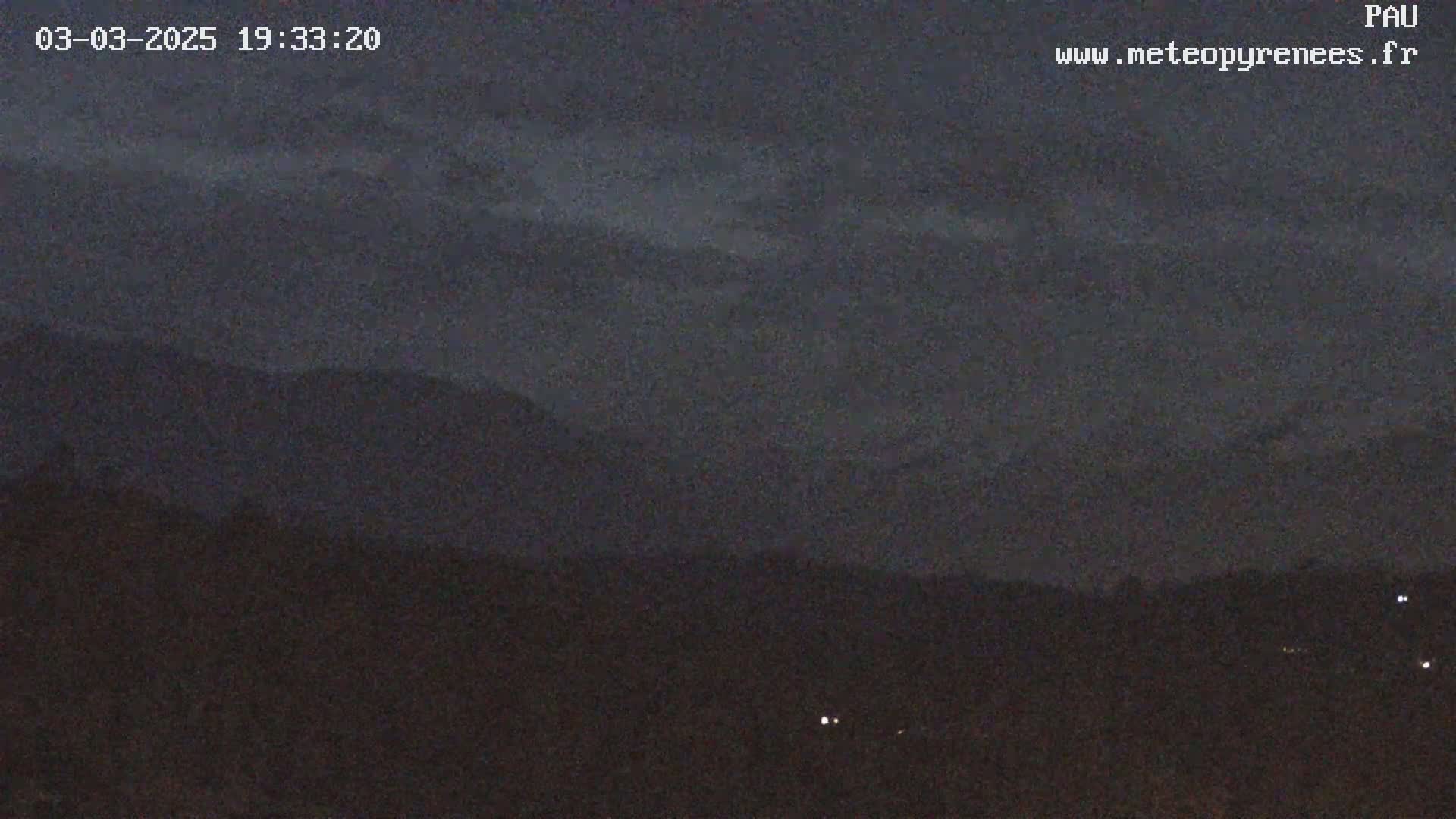 A nighttime, overcast view shows dark mountains in the distance and a flat, dark foreground.