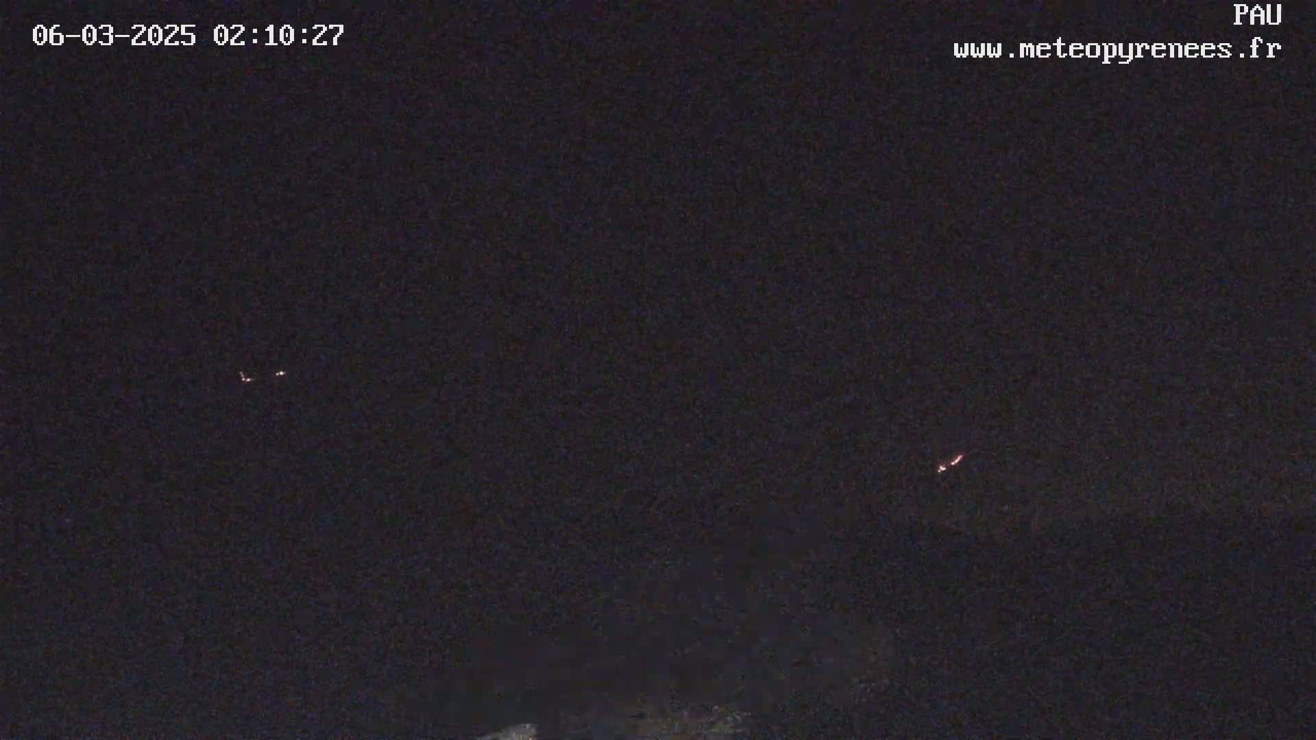 A nighttime long shot shows faint lights in the dark sky above a dark landscape.