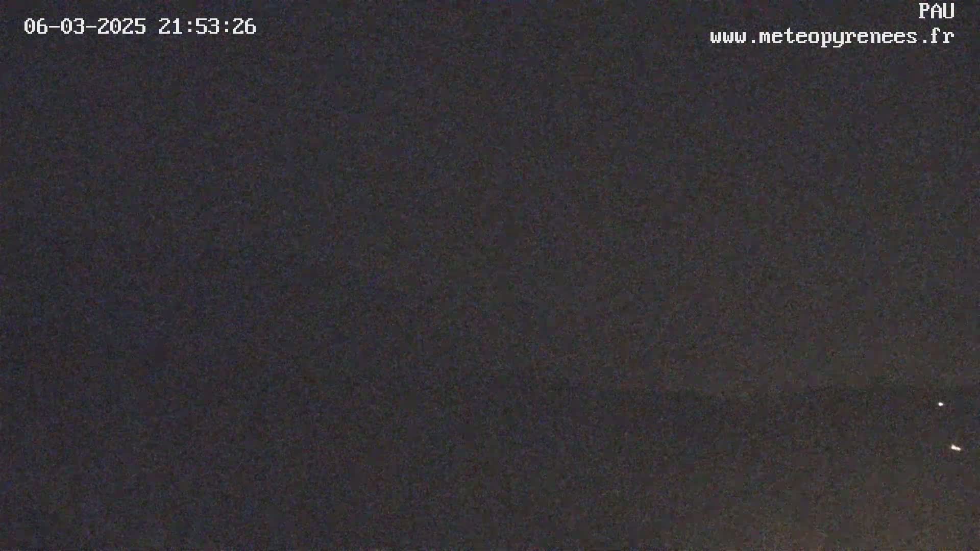 A nighttime image shows a dark, mostly clear sky with a few faint lights visible on the horizon.