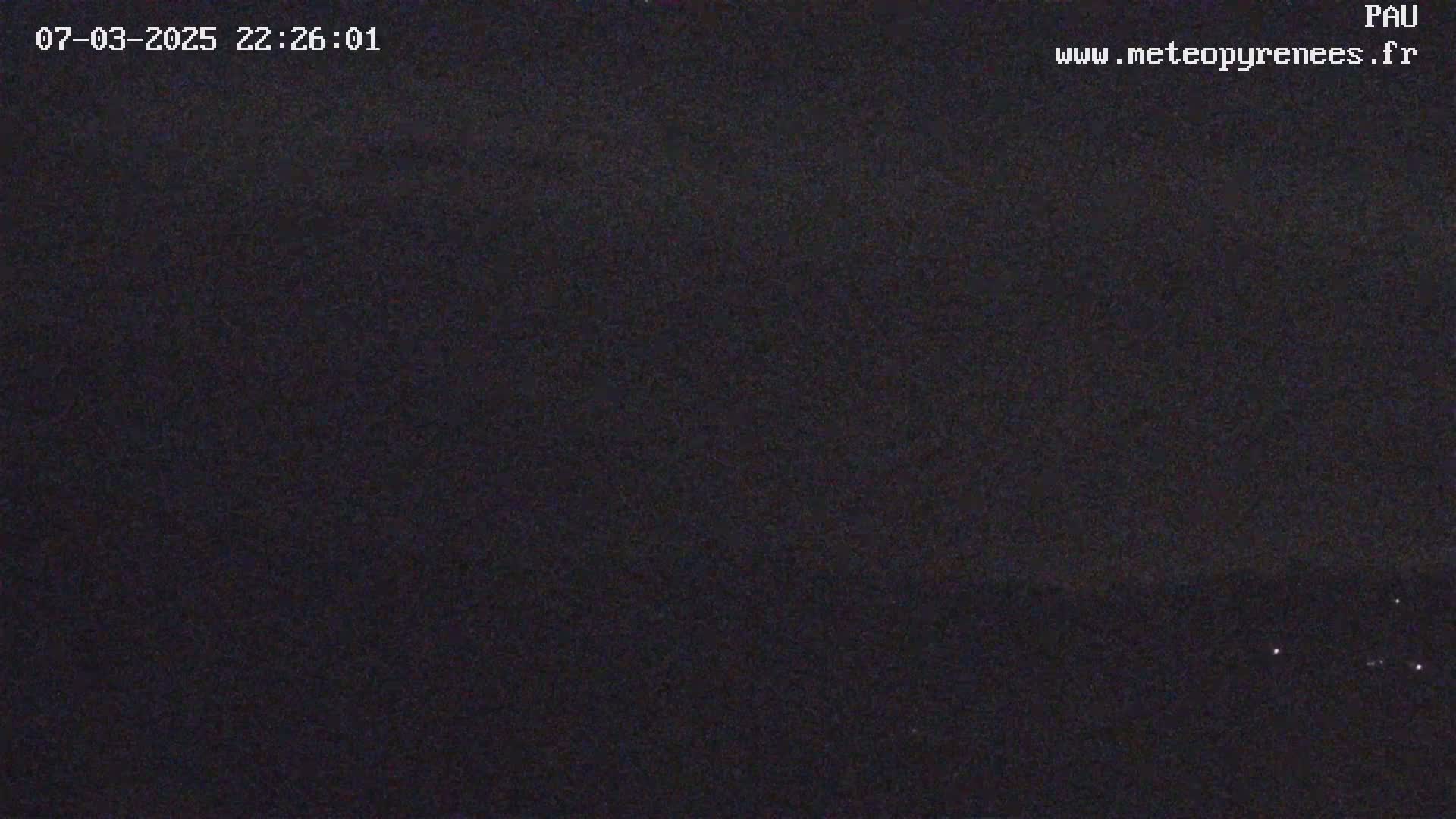 A nighttime, dark image shows a few faint lights on the horizon.