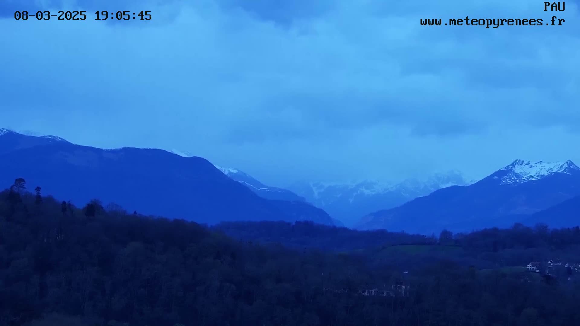 Snow-capped mountains are visible in the distance, under a twilight sky, above a landscape of dark green hills and trees.