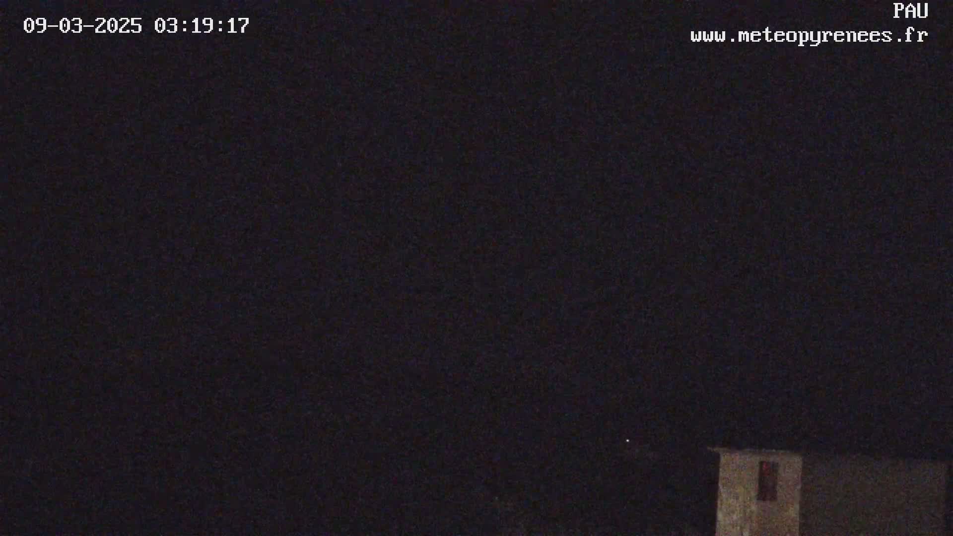 A nighttime, dark outdoor scene shows a small building under a clear, starlit sky.