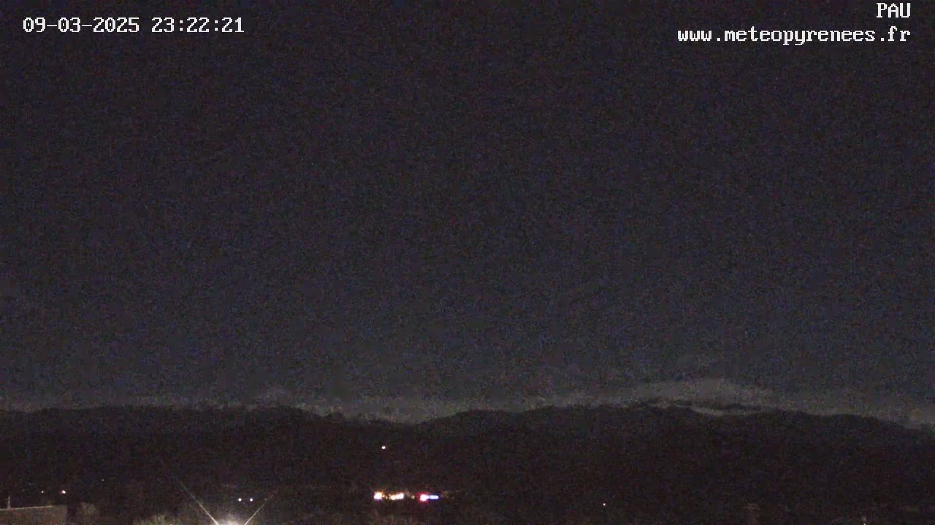 A nighttime long shot shows a dark, mostly clear sky over a distant mountain range under a slightly cloudy sky.
