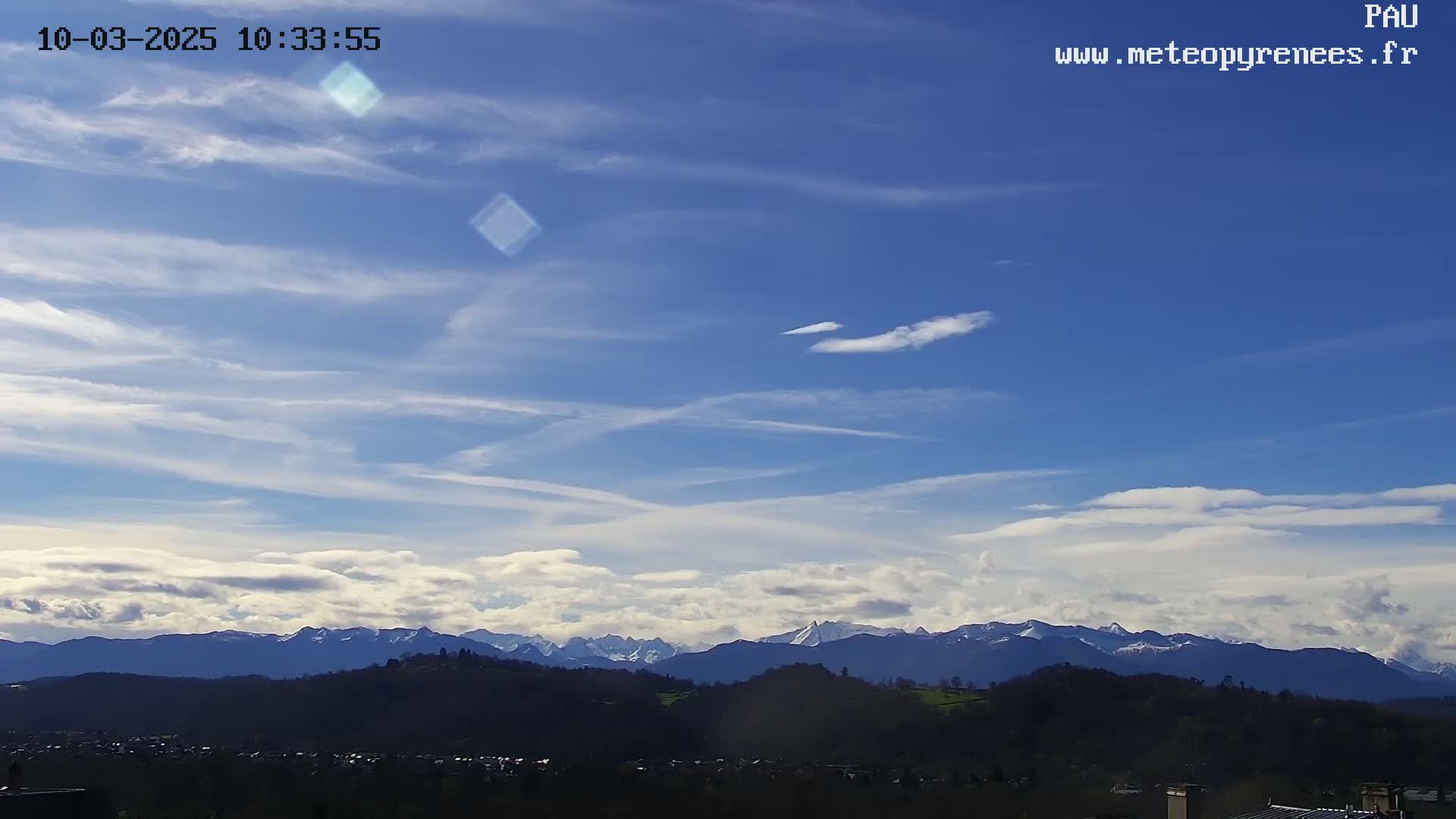 A mostly clear blue sky with thin, wispy clouds and a layer of low clouds over a distant mountain range.