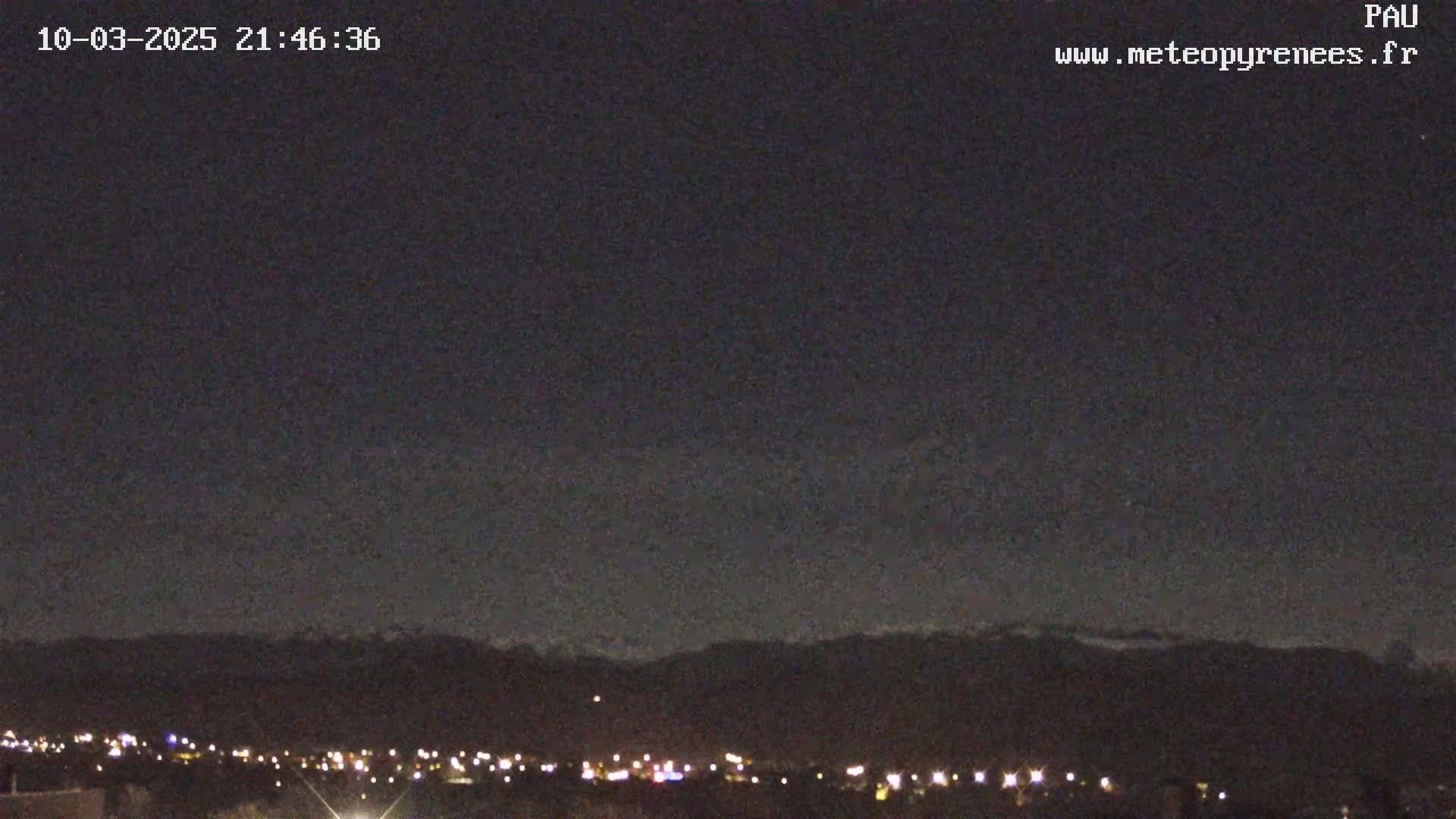A nighttime view shows a dark sky over a city with lights, and distant mountains silhouetted against the horizon.