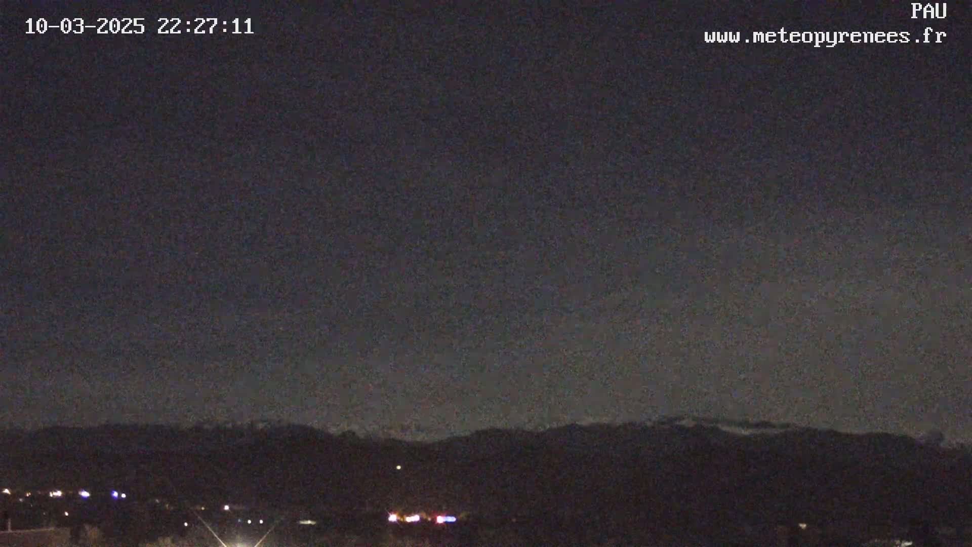 A nighttime view shows a dark sky over a distant mountain range with a few scattered lights visible in the foreground.