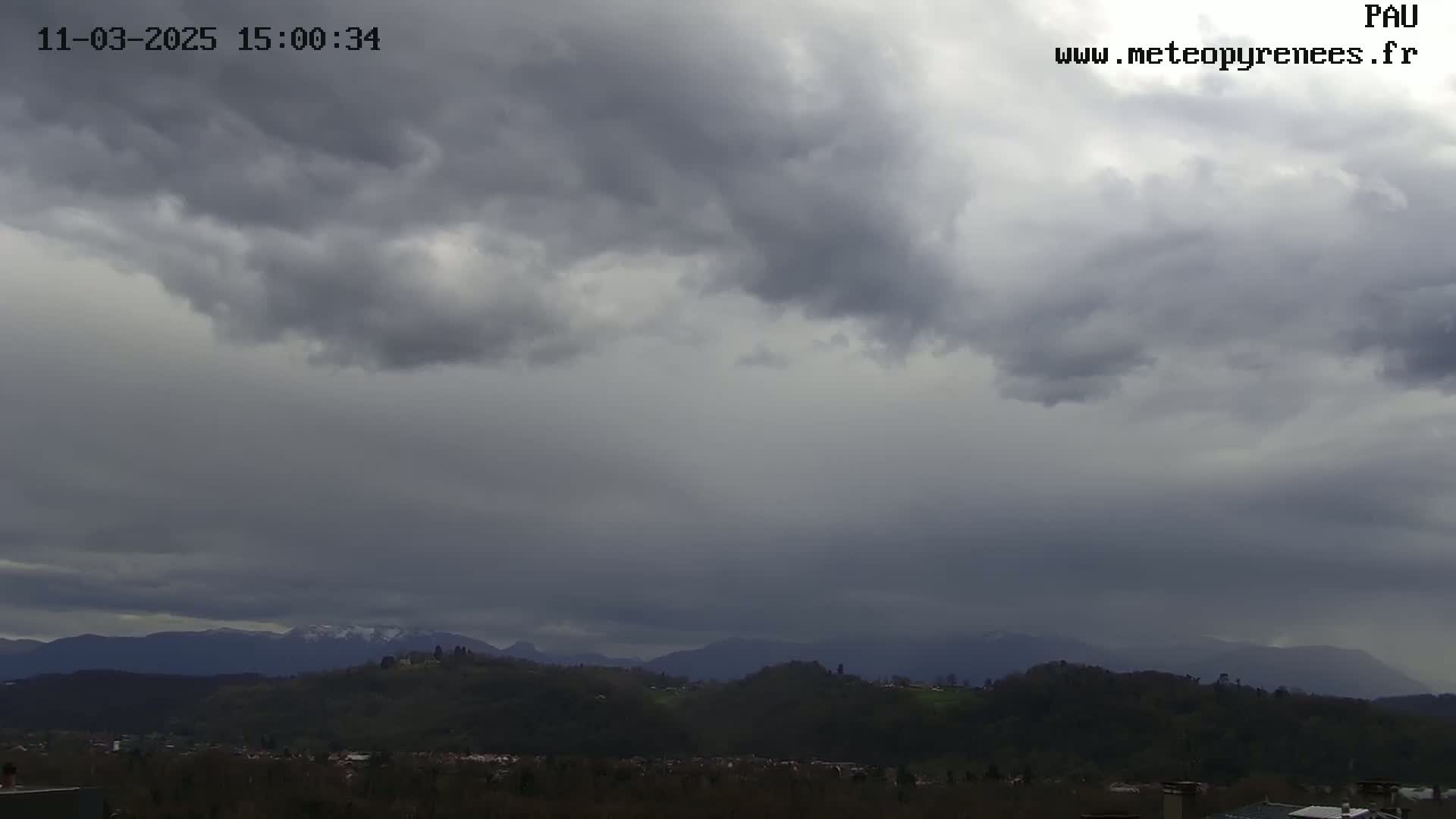 Overcast skies loom over a landscape of rolling green hills and distant mountains with snow-capped peaks.