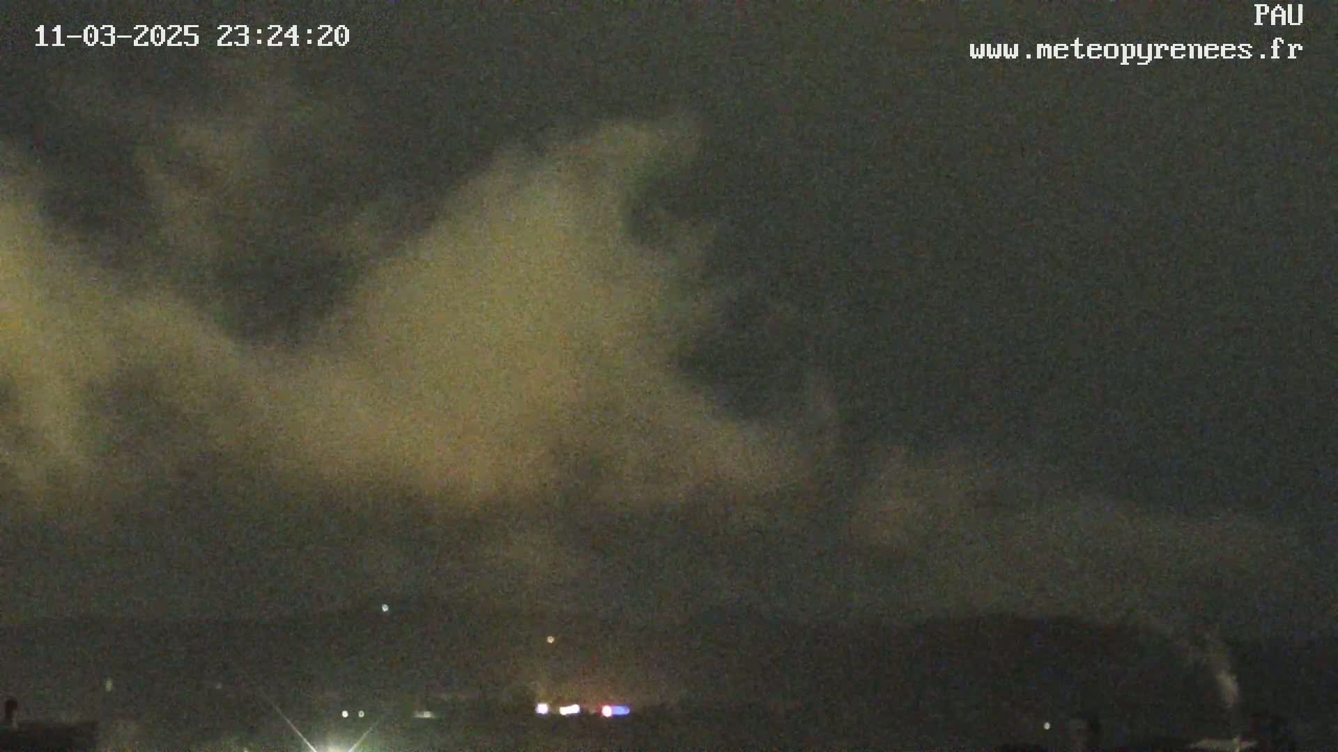 A nighttime scene of a cloudy sky over a dark landscape with a few faint lights visible in the distance.