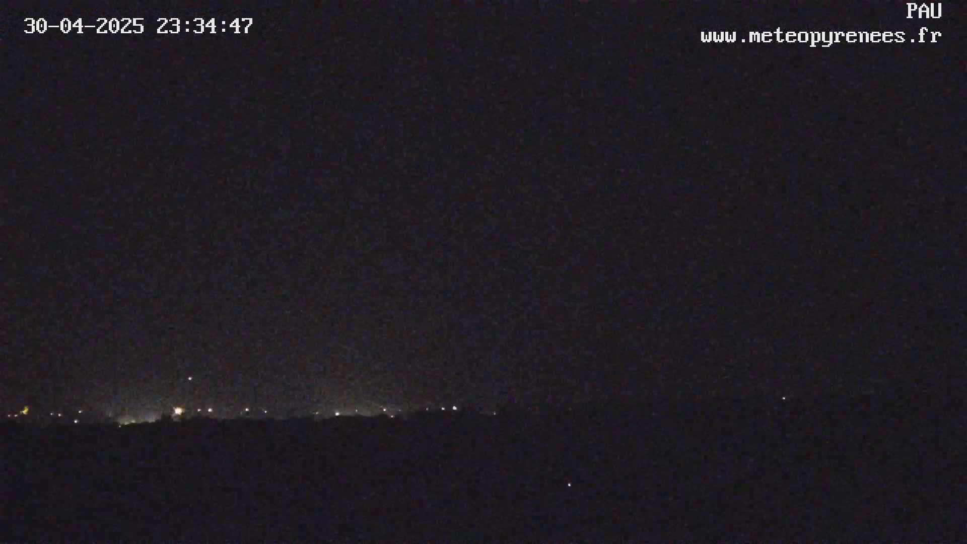A nighttime long shot shows a dark landscape with a faint line of distant lights under a clear, dark sky.