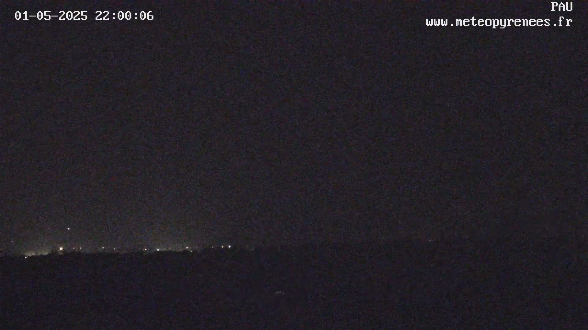 A nighttime view shows a dark landscape with a faint line of lights on the horizon under a clear, dark sky.