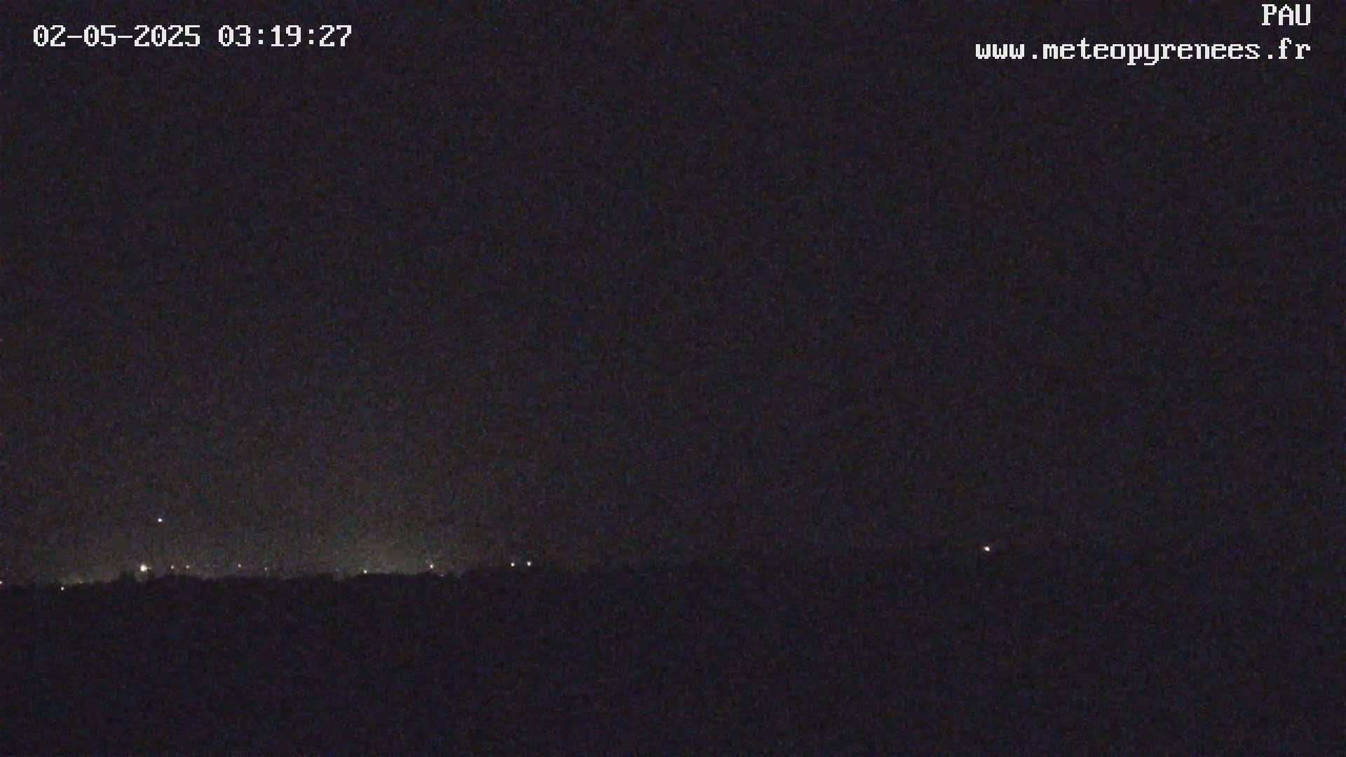A nighttime, dark landscape is visible with a few distant lights on the horizon under a clear, dark sky.