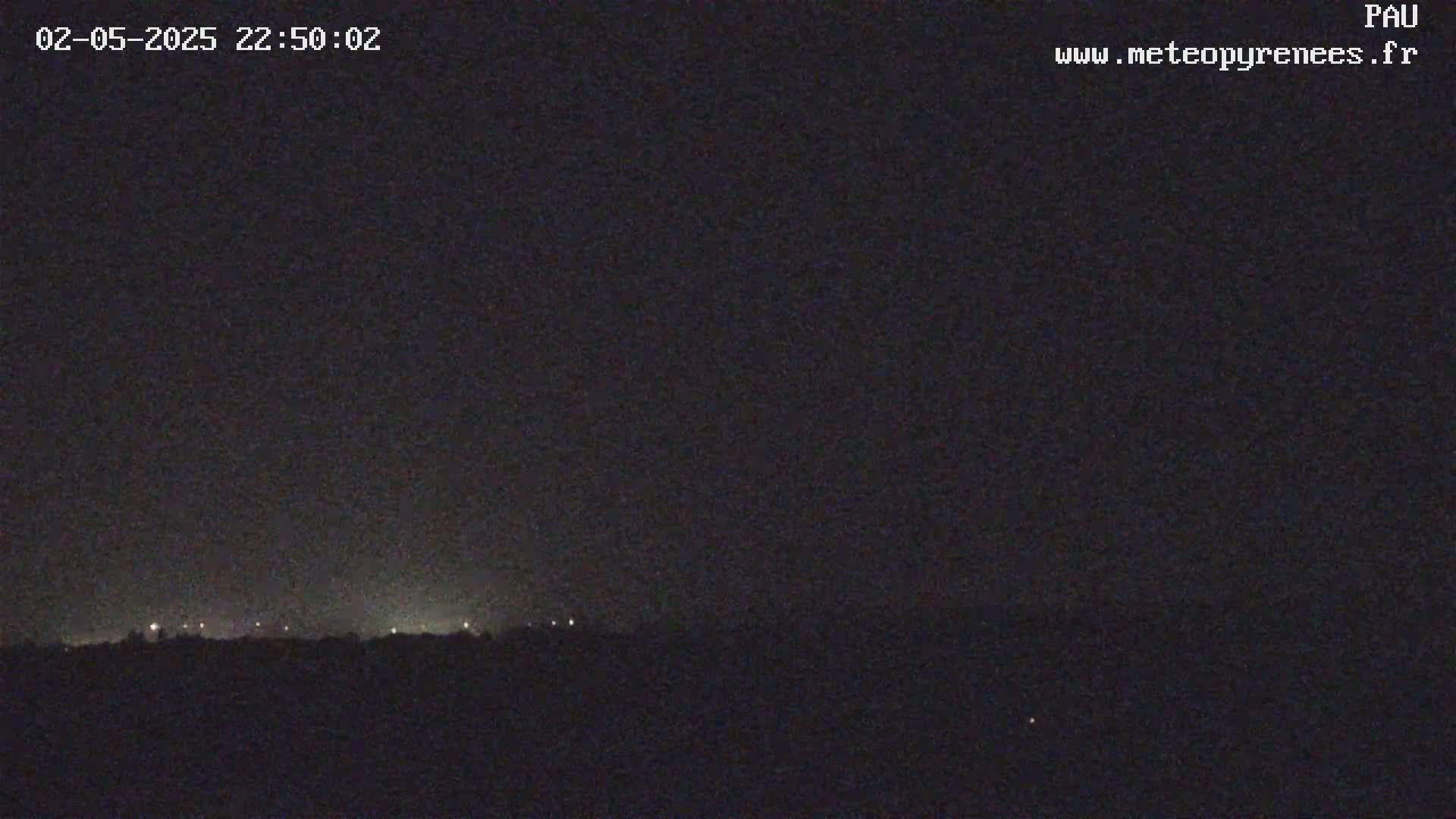 A dark, nighttime landscape shows a distant line of lights on the horizon under a clear, dark sky.