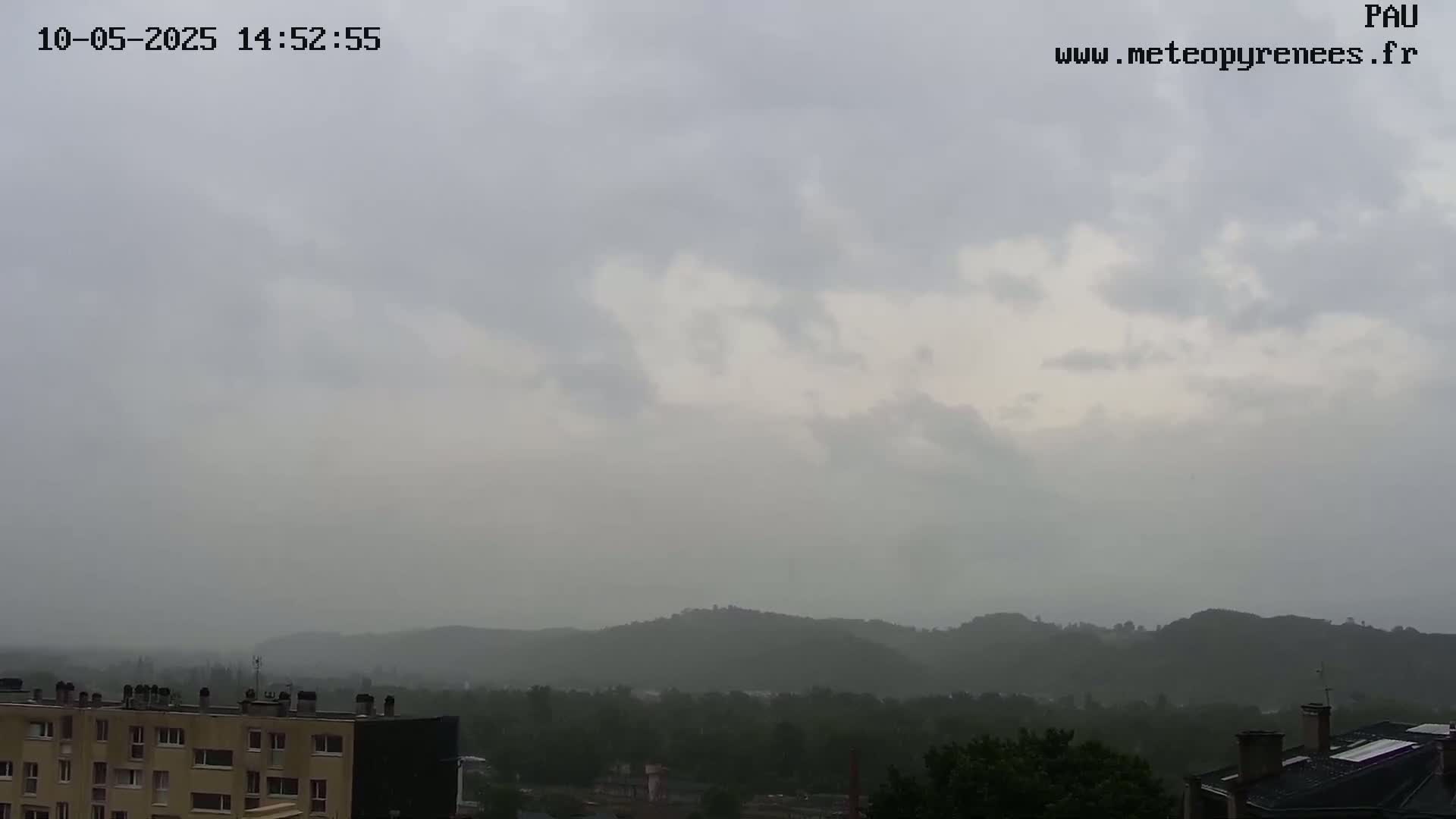 A hazy, overcast sky hangs over a cityscape and distant hills under a light rain.