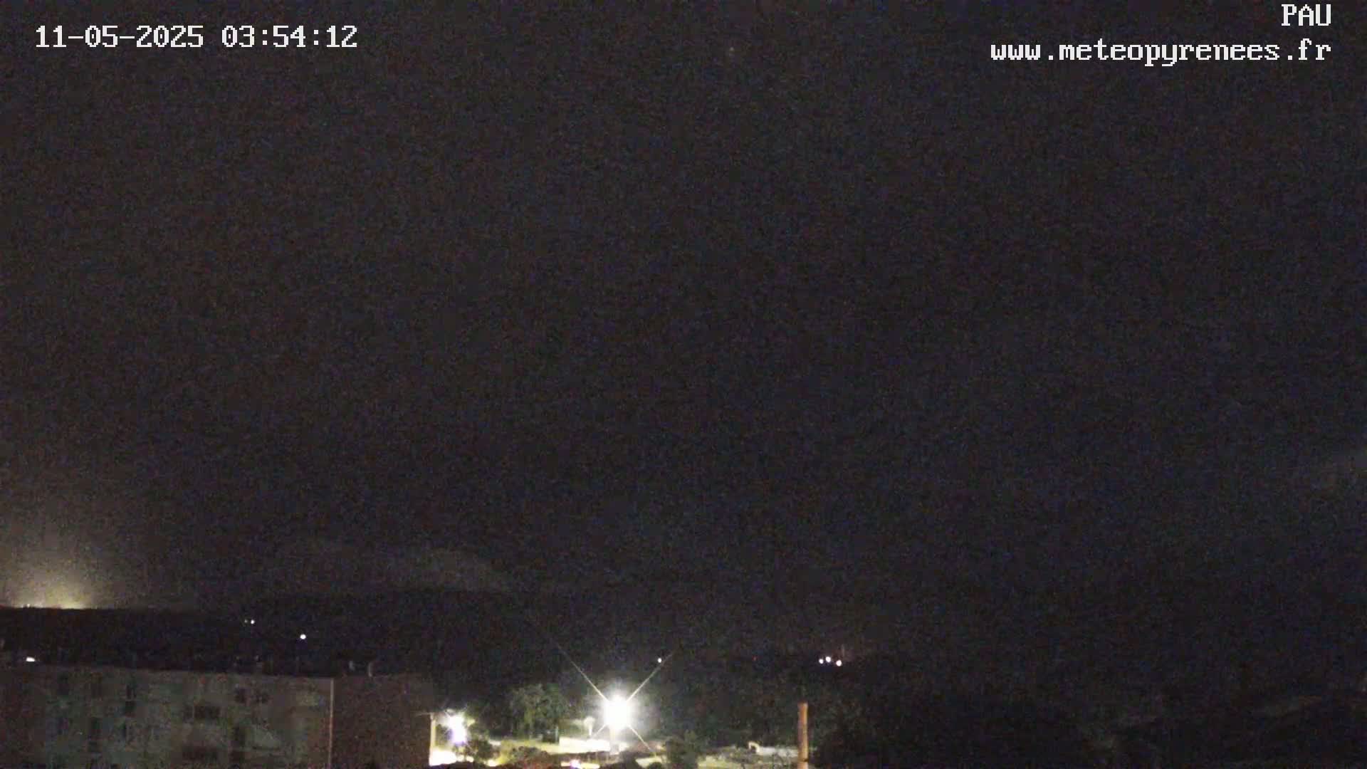 A nighttime view of a city with buildings and some trees, under a dark, mostly clear sky.