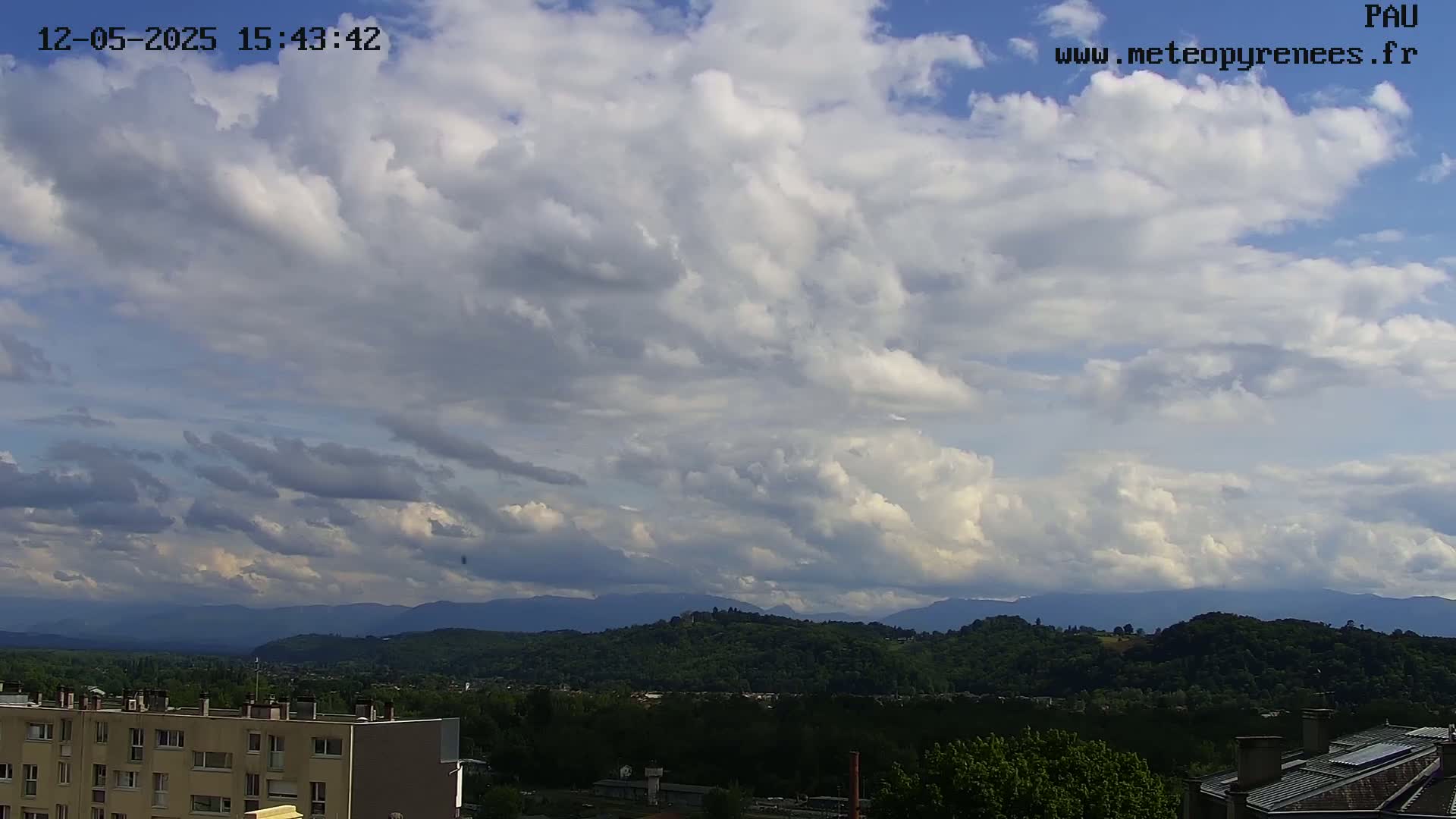 A partly cloudy sky overlooks a hilly landscape with a city and buildings in the foreground.