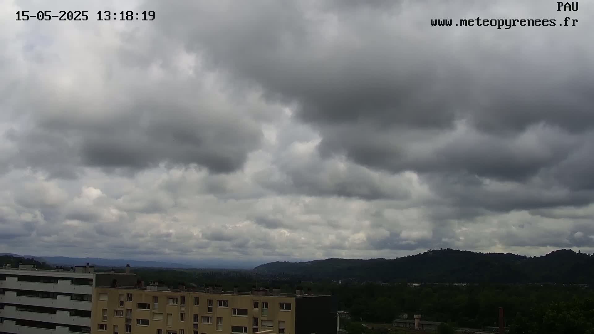 Overcast skies loom over a city landscape of low-rise buildings and distant hills.