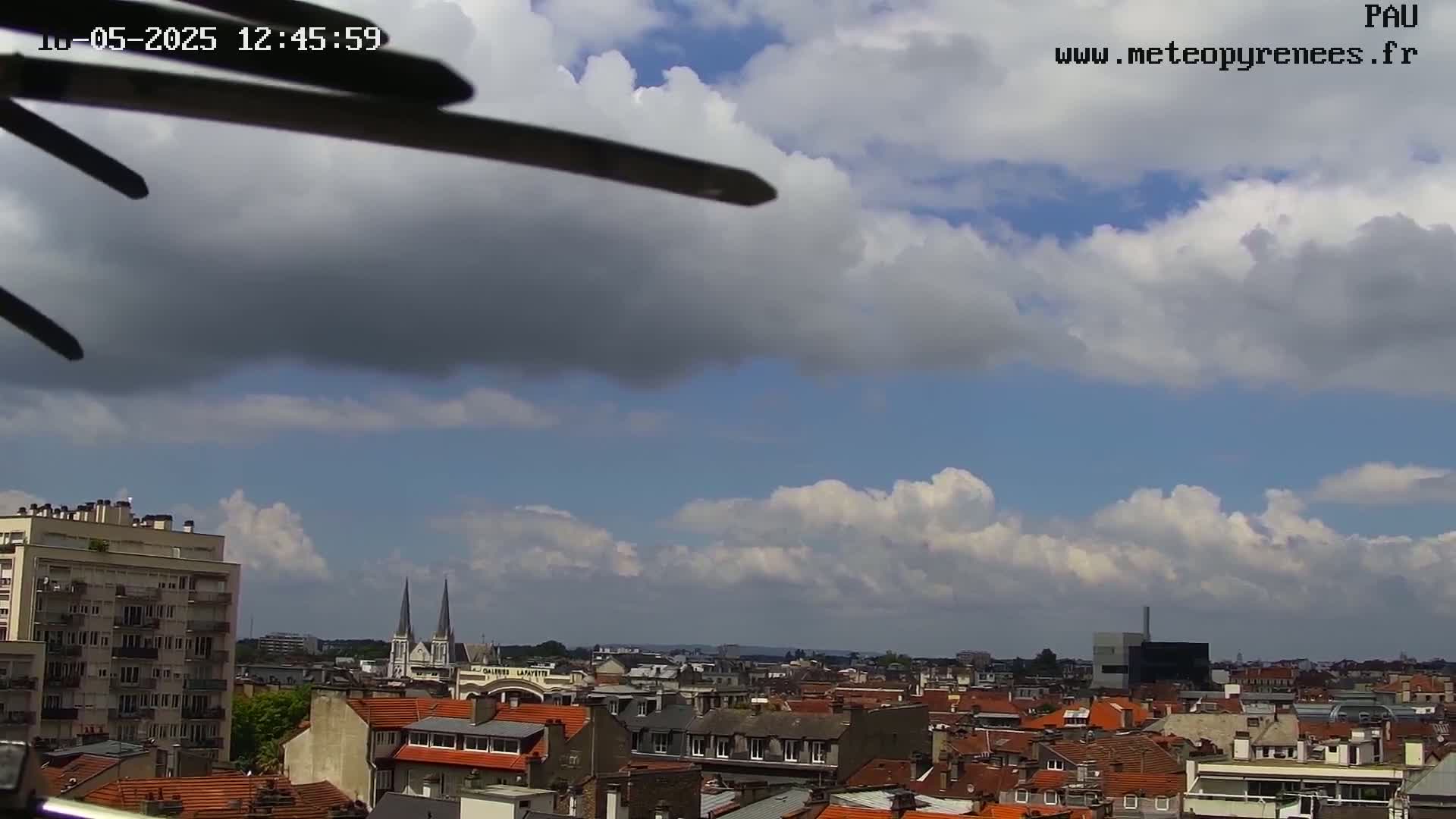 A partly cloudy sky overlooks a city with red-tiled roofs, tall buildings, and church spires.