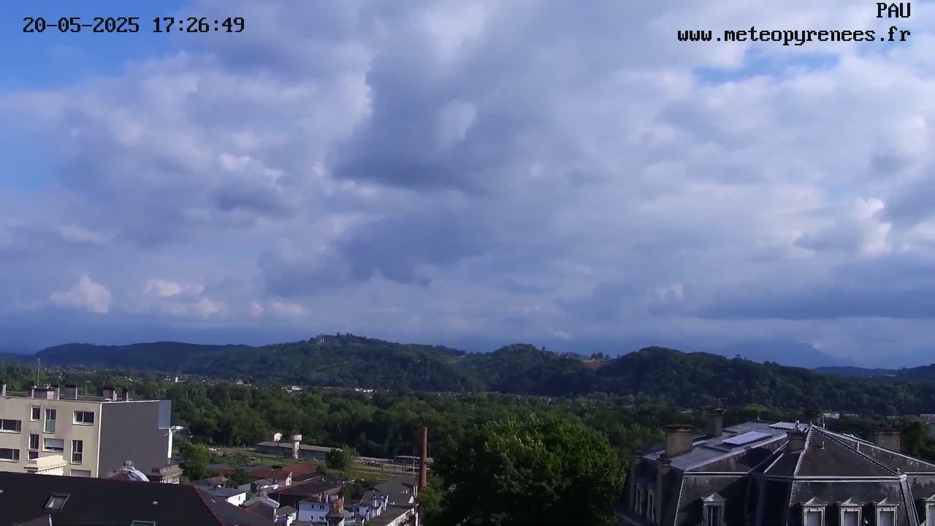 A partly cloudy sky overlooks a town nestled amongst green hills.