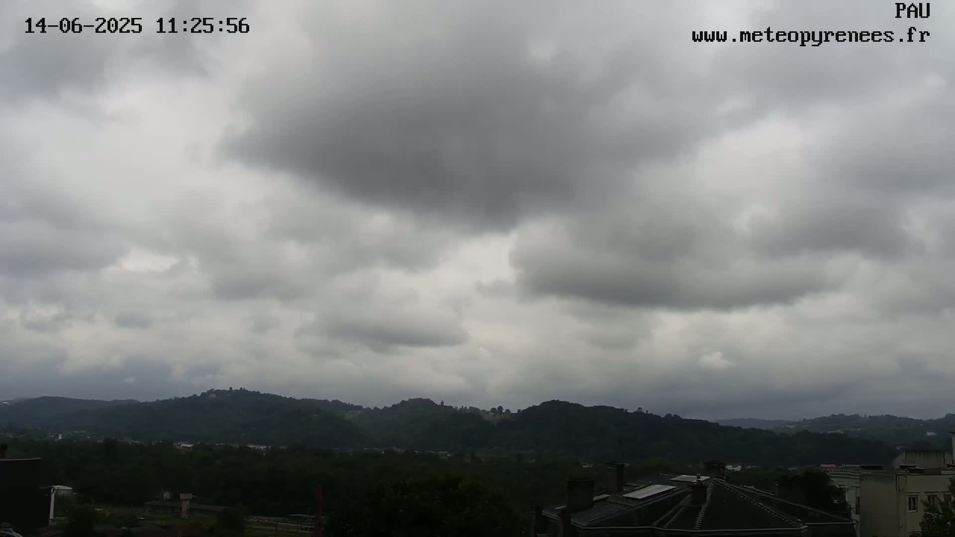 A view of overcast skies over a hilly landscape with buildings visible in the foreground.