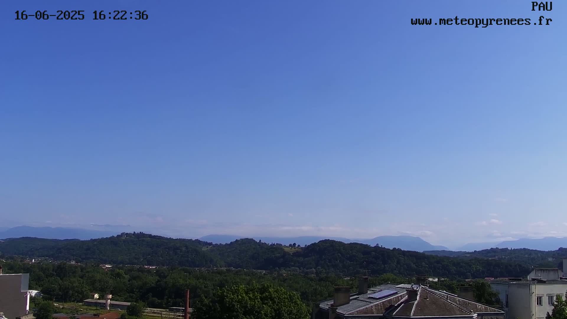 A clear blue sky overlooks a landscape of green hills and distant mountains, with buildings visible in the foreground.