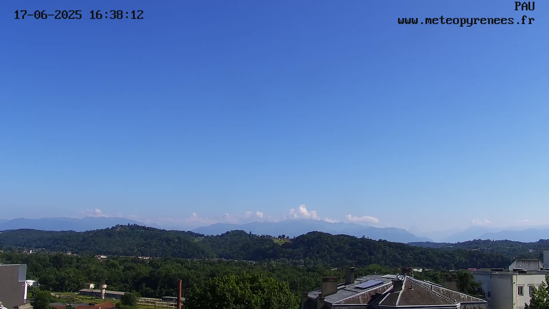 A mostly clear blue sky overlooks a landscape of green hills and distant mountains.