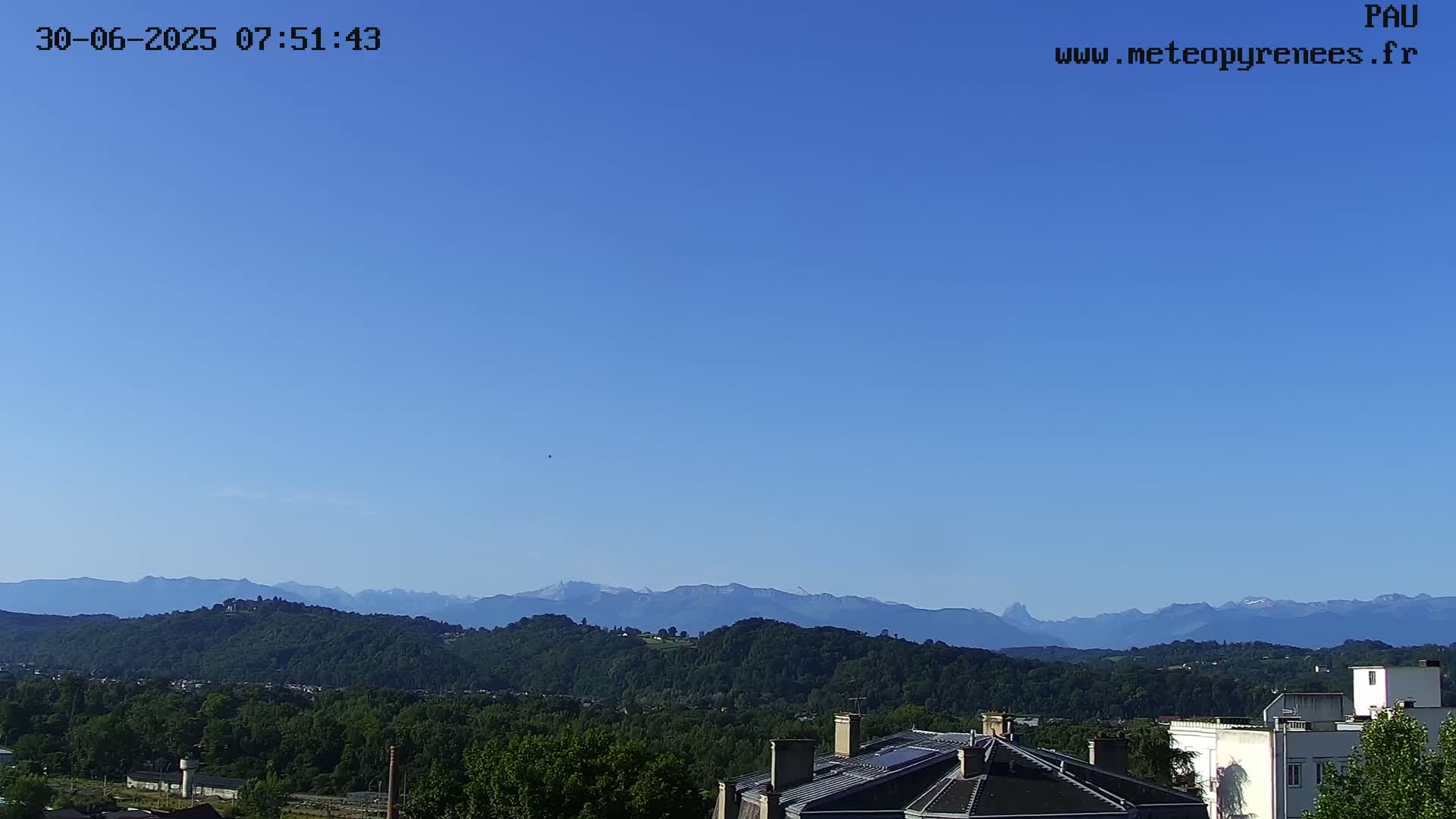 A clear blue sky overlooks a green, hilly landscape with distant mountains.