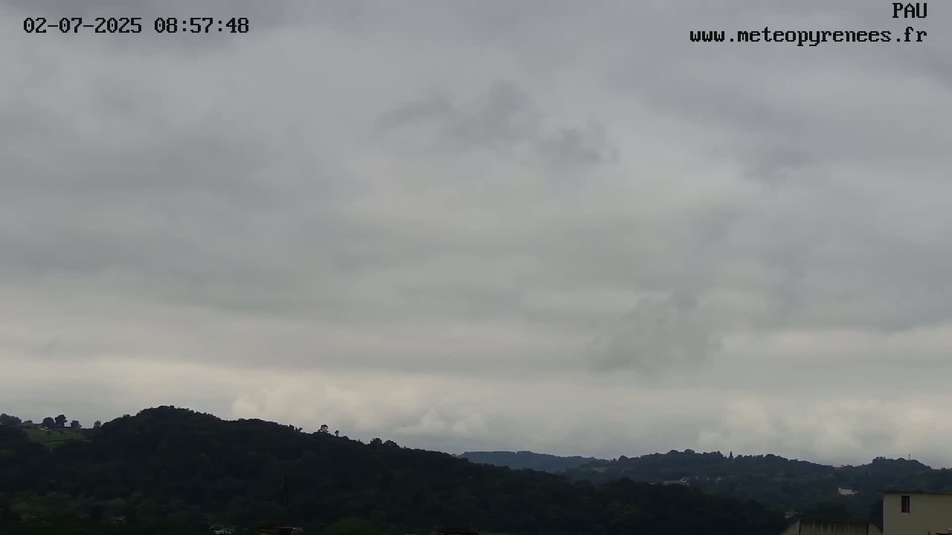 A mostly cloudy sky hangs over dark green hills and a distant cityscape.