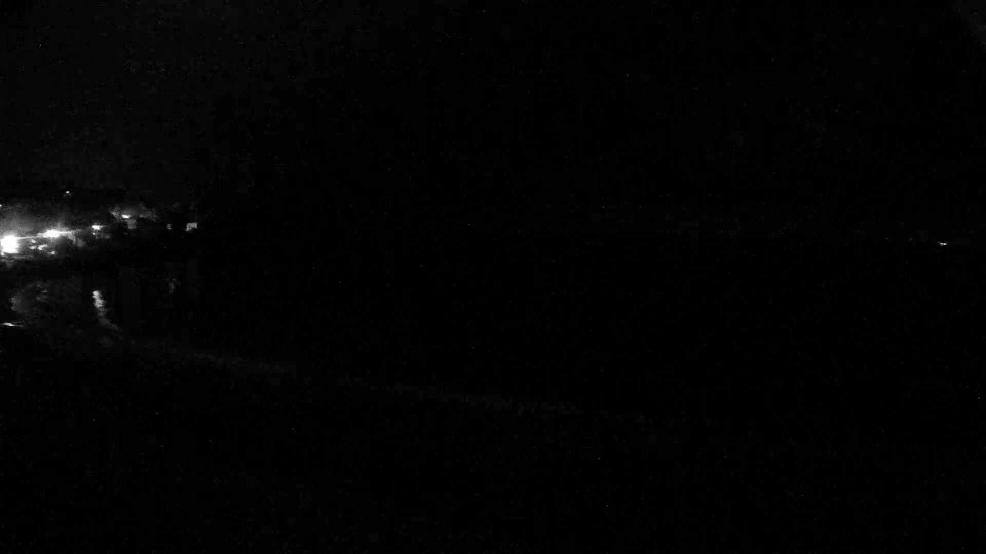 A nighttime, low-light image shows a dark landscape with faint light sources in the distance and possibly some clouds.