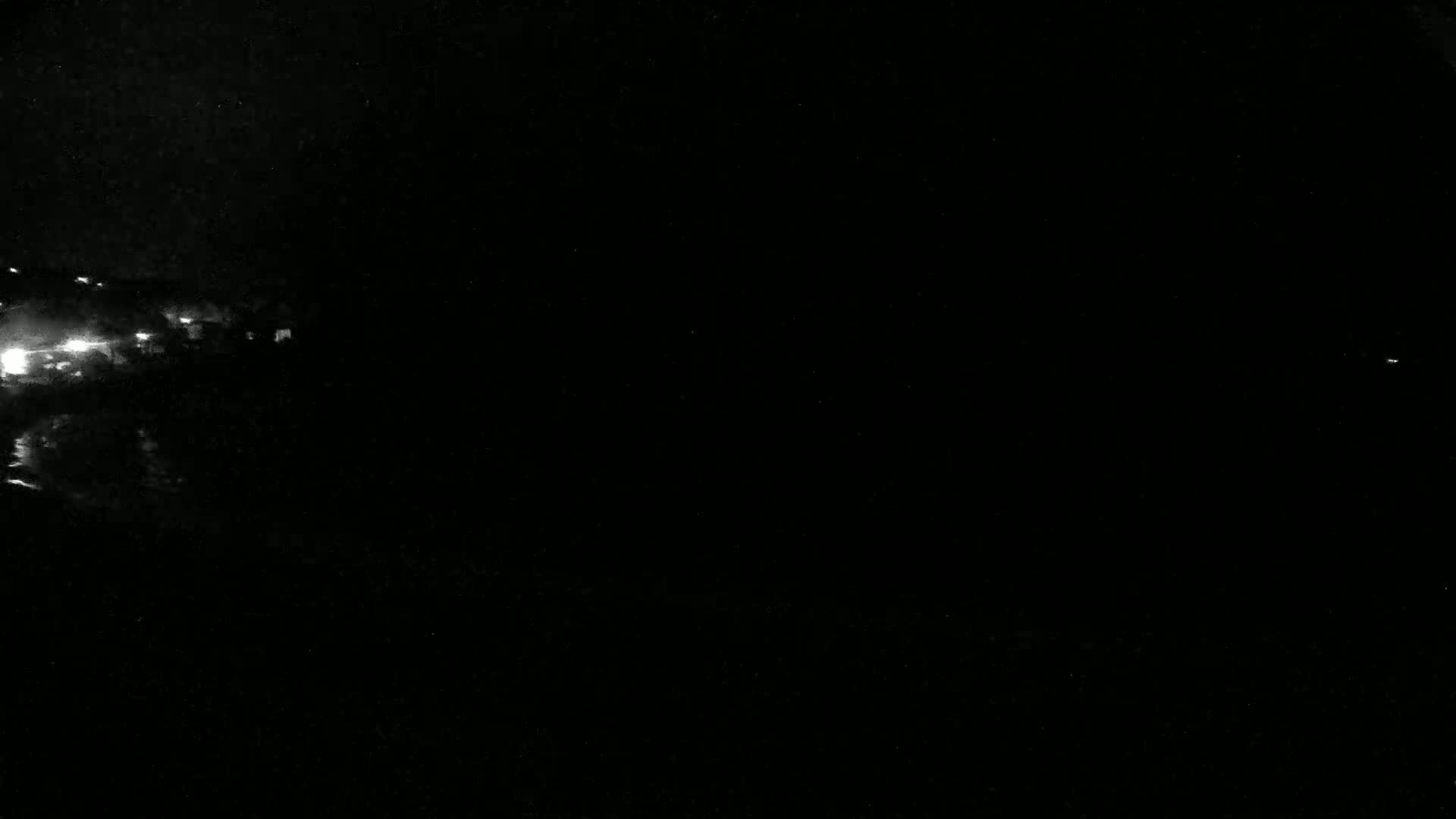A nighttime scene shows a cluster of faint lights in the distance on the left, against a completely dark background.