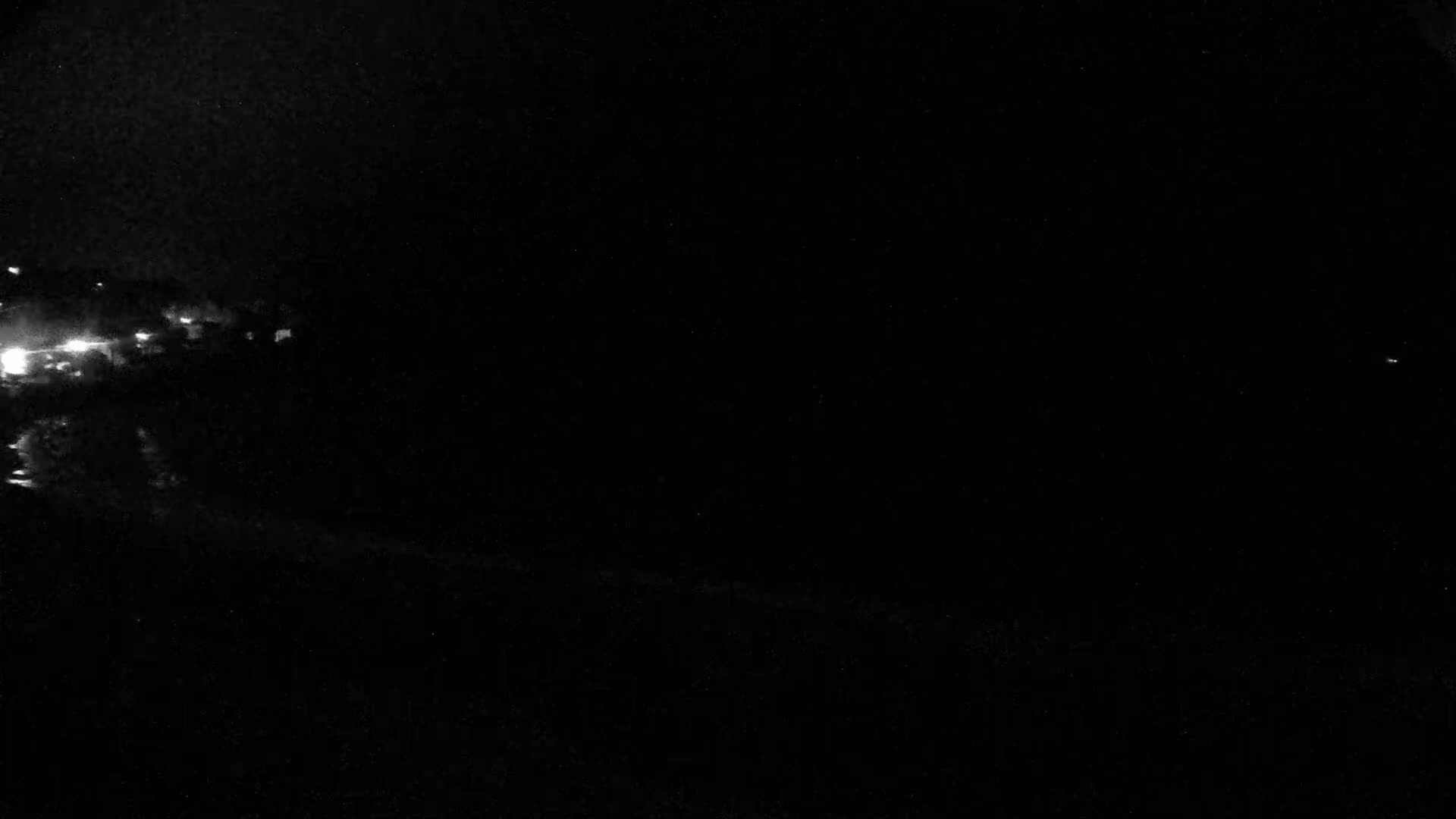 A nighttime, low-light view shows a dark landscape with a few faint lights visible in the distance.