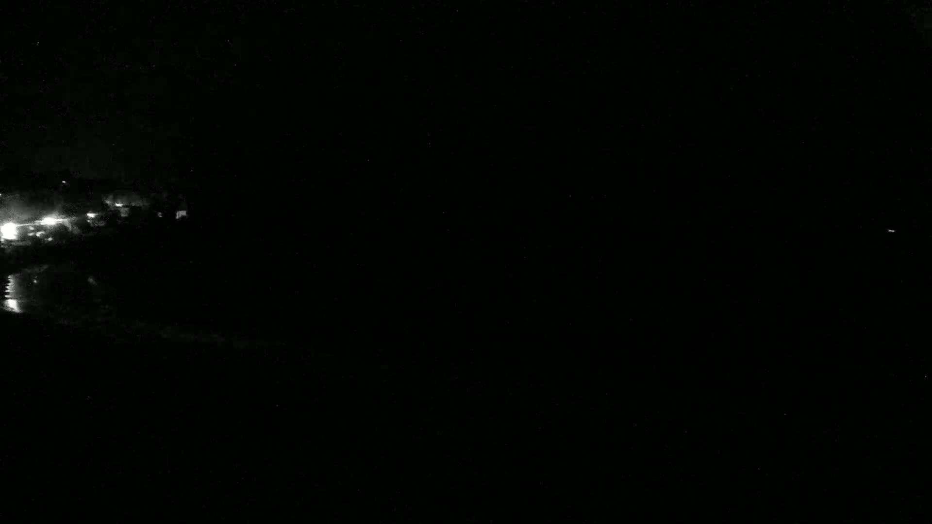 A nighttime view shows a dimly lit shoreline with a few lights visible in the distance.