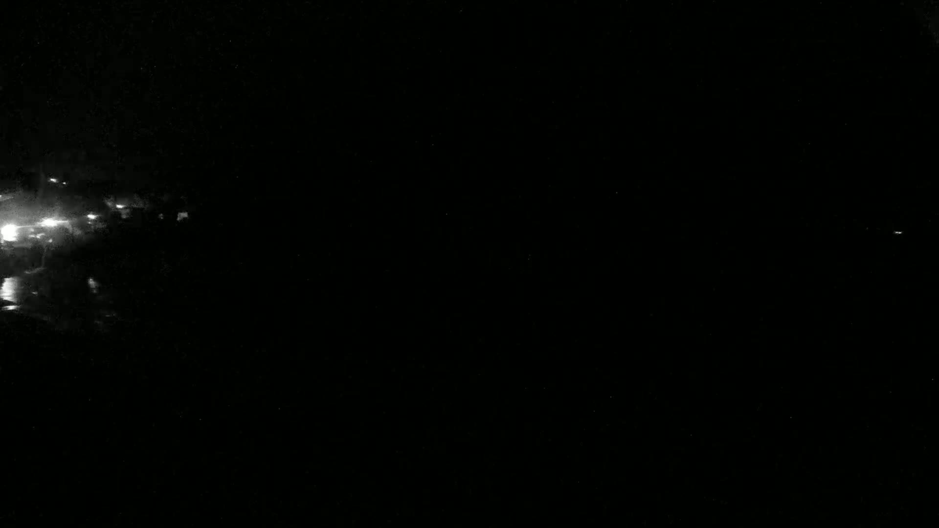 A nighttime, low-light image shows a blurry cluster of lights in the left corner, possibly from a distant city or town, against a mostly dark background.