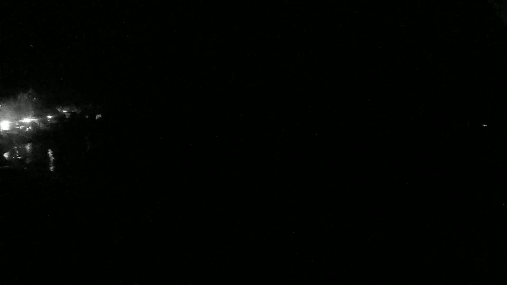 A nighttime image shows bright, blurry lights on the left, possibly distant city lights, against a completely dark sky.